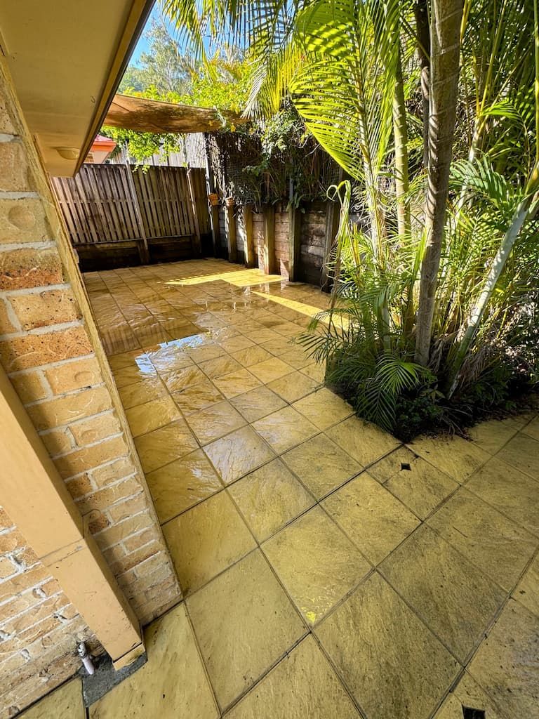 A patio with a brick wall and trees in the background.