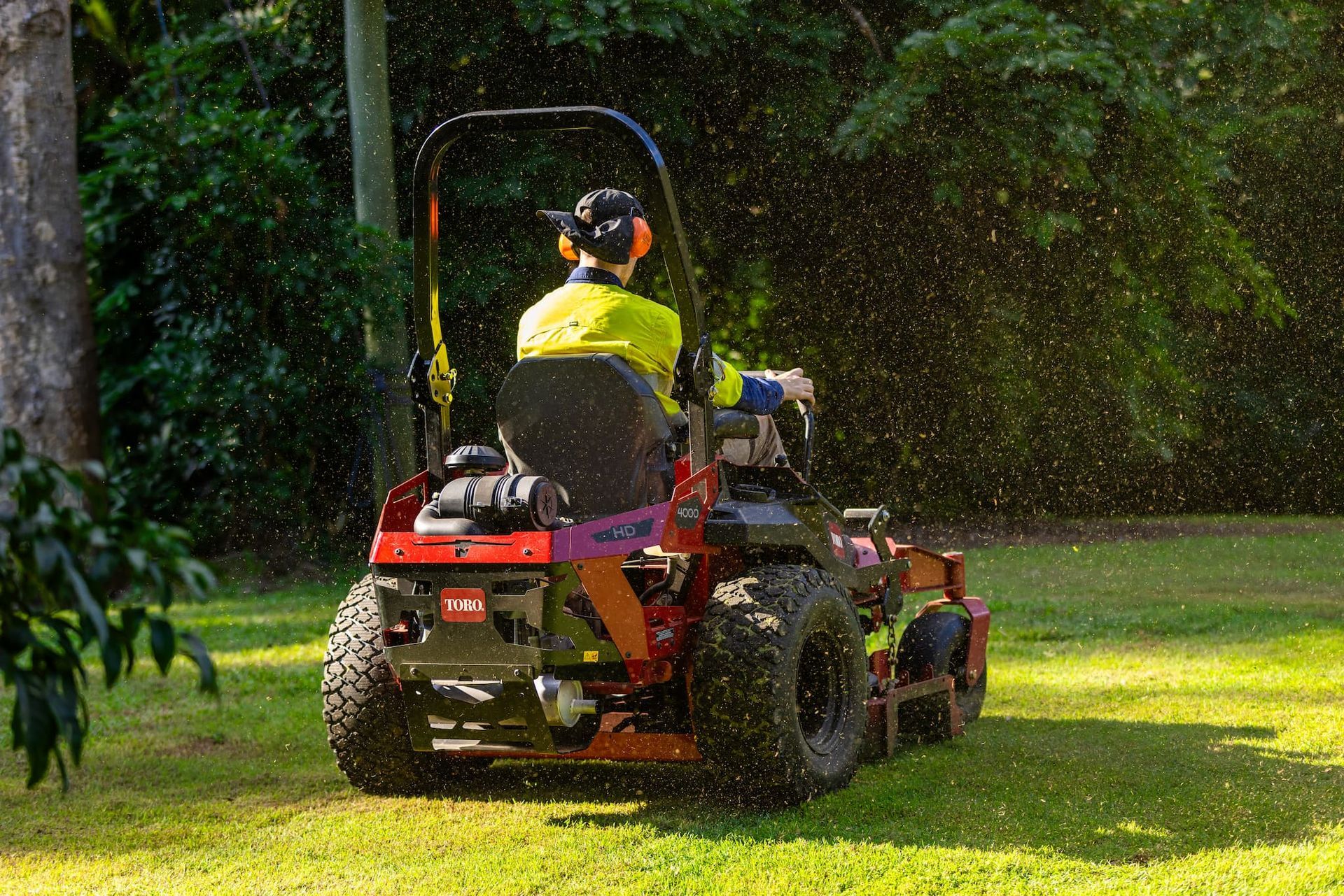A man is riding a lawn mower on a lush green lawn in Taringa