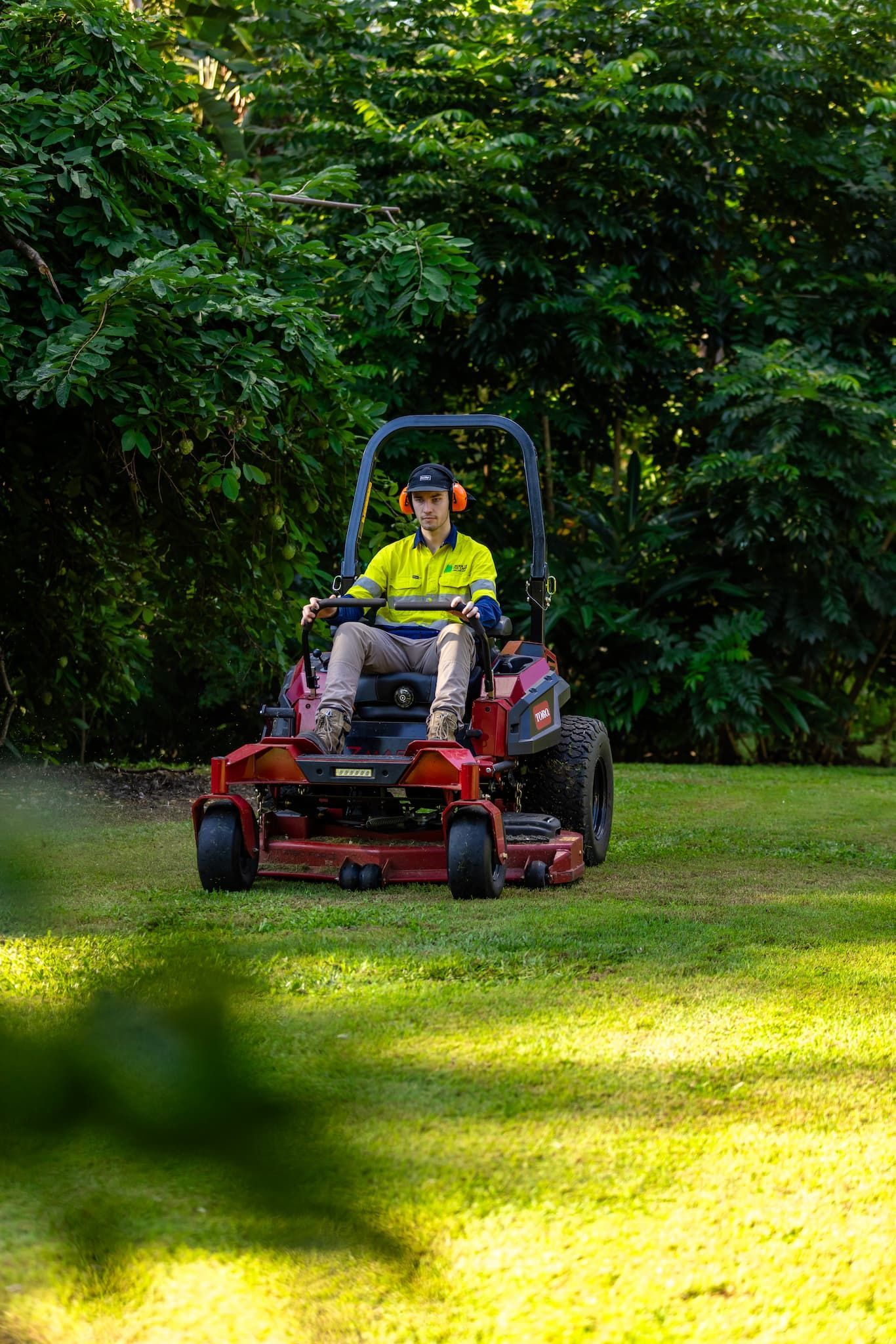 Person mowing a lawn on a red riding mower in a yard with green grass and trees.