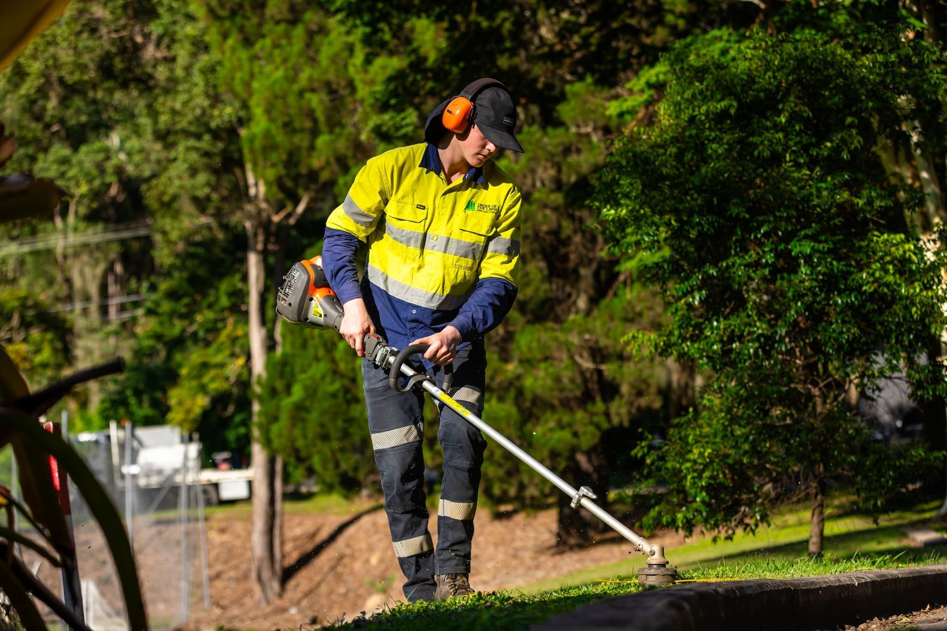A man is cutting grass with a lawn mower in a park in Taringa