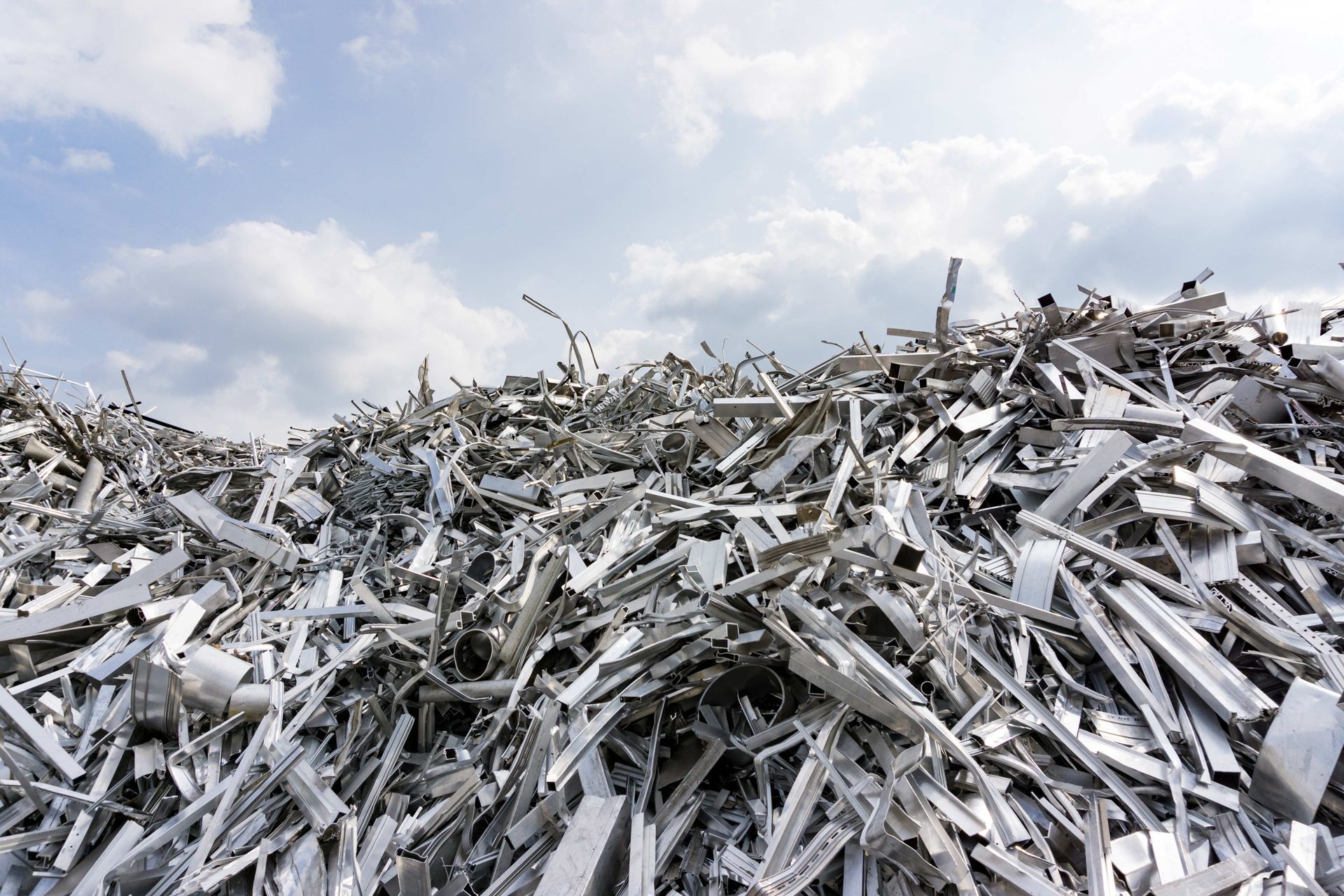 A pile of aluminium scrap metal against a blue sky with clouds.