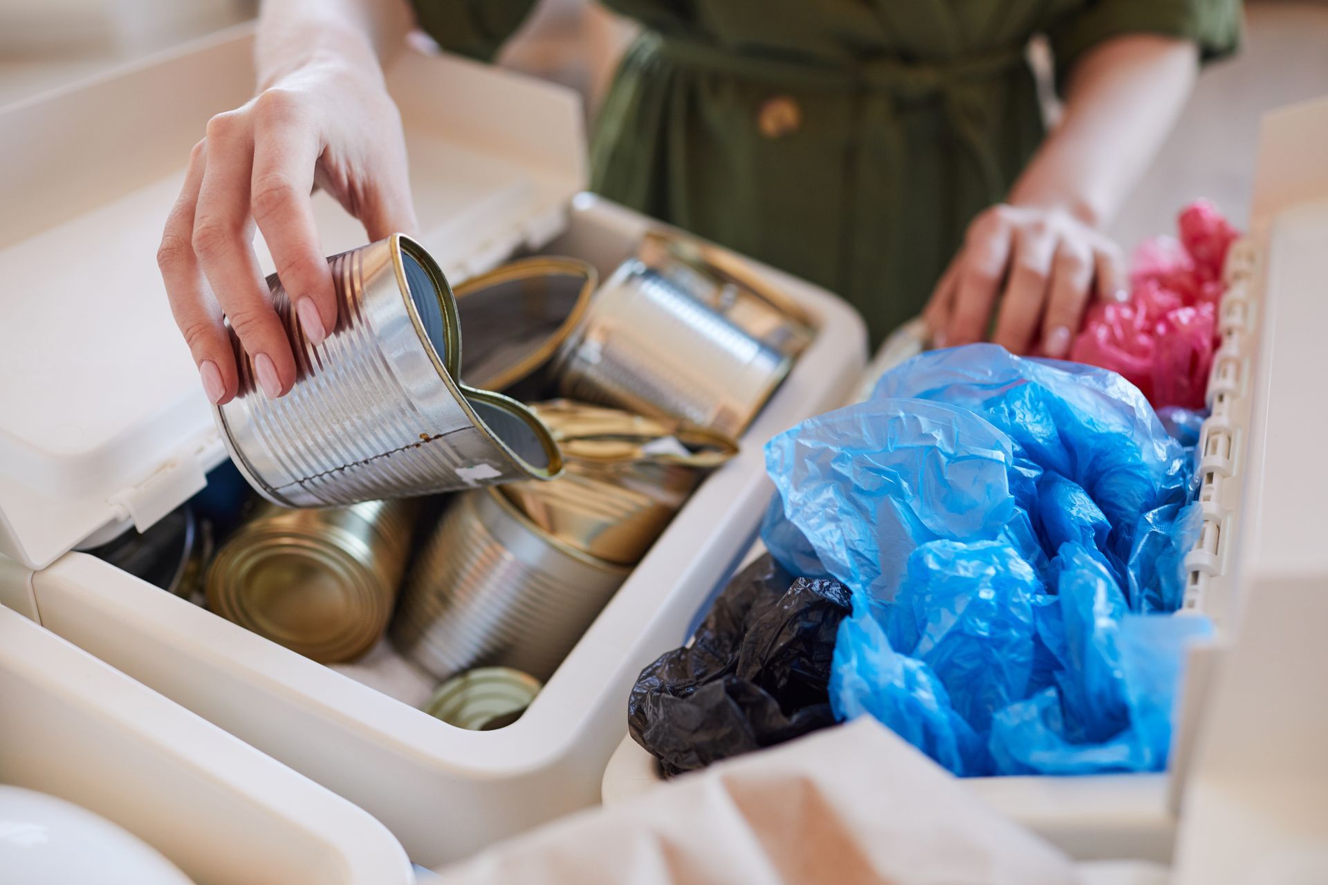Person sorting recyclable materials, placing a metal can into a bin, with plastic bags visible.