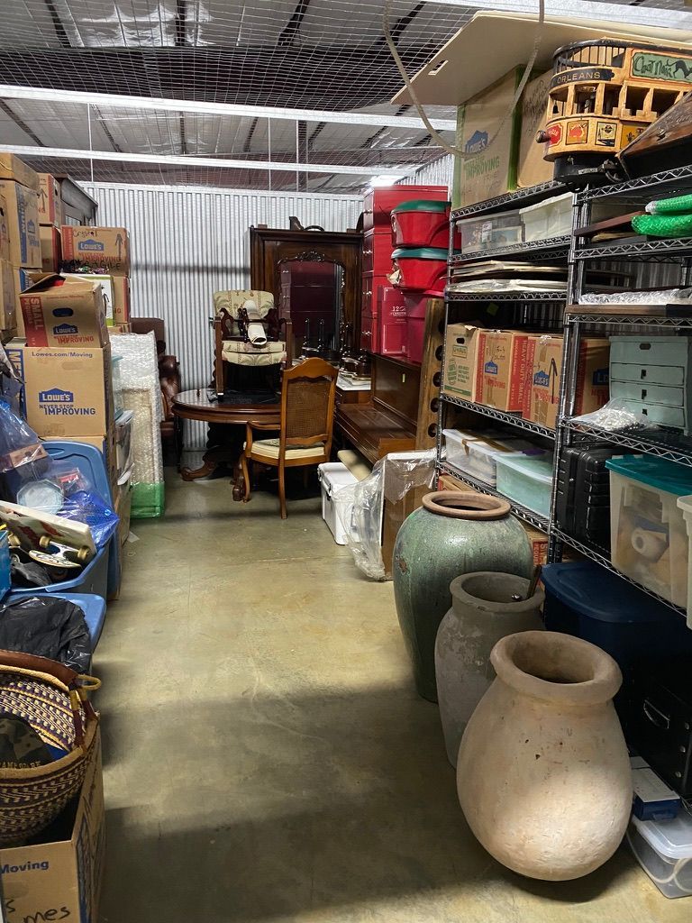 Storage unit filled with furniture, boxes, and various items. Interior view, shelves on right, vases in foreground.
