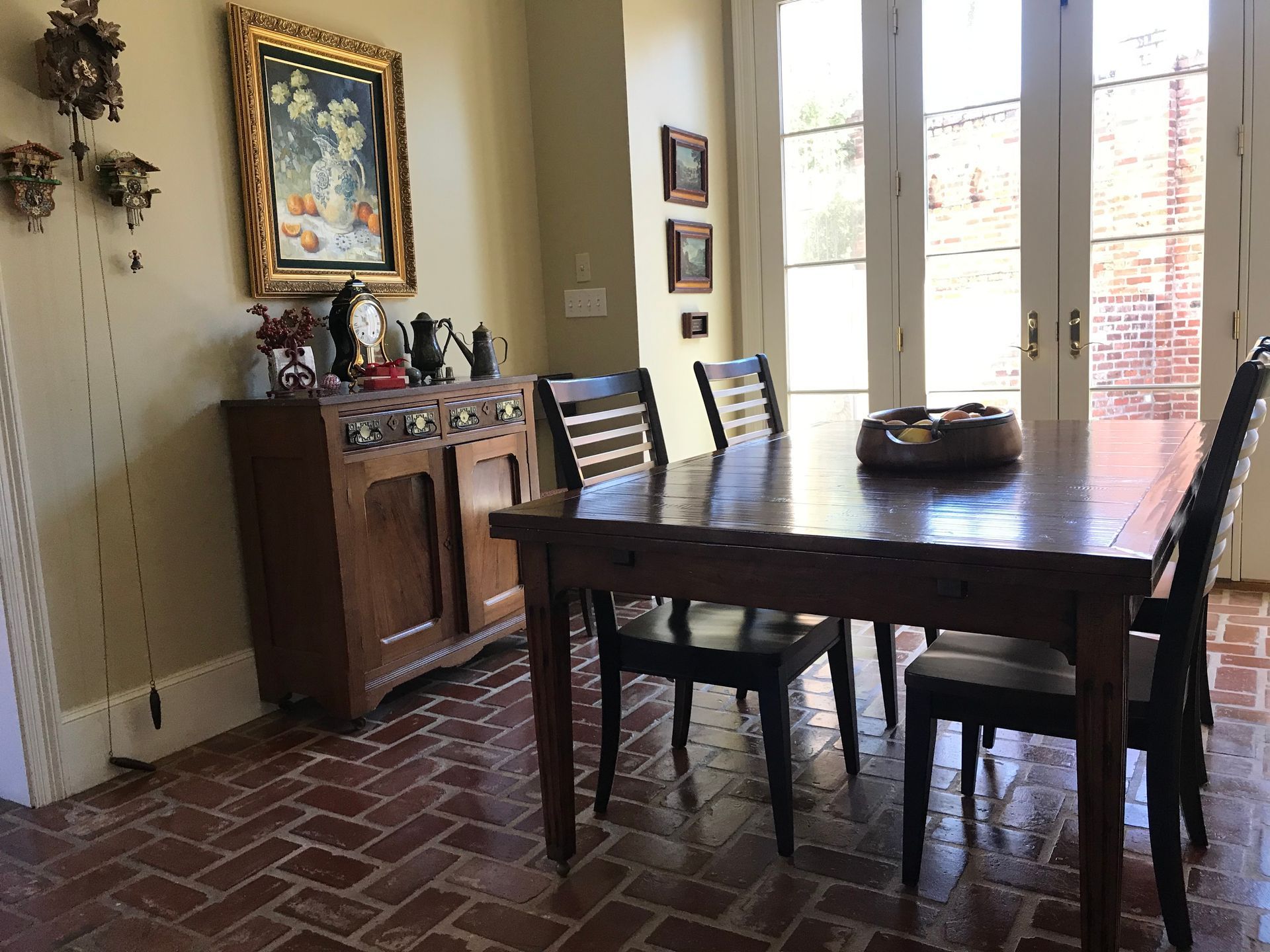 Dining room with table and chairs, cabinet with art, brick floor, French doors.