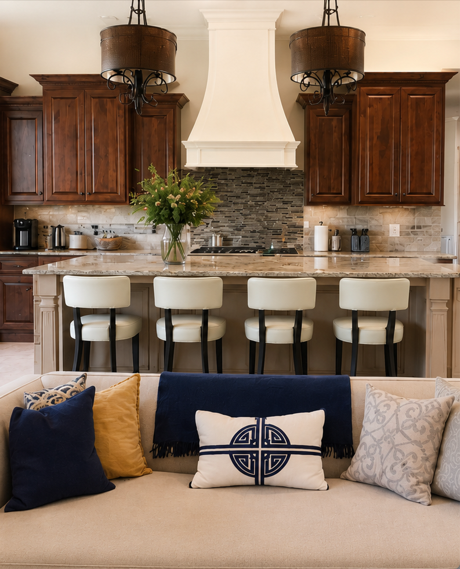 Stylish kitchen with dark wood cabinets, stone backsplash, island stools, and a beige sofa in the foreground