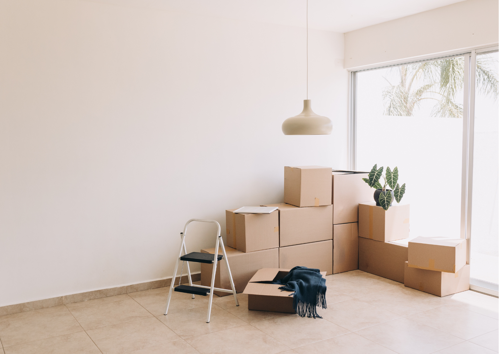 Empty room with cardboard boxes stacked, a small ladder, and a hanging light.