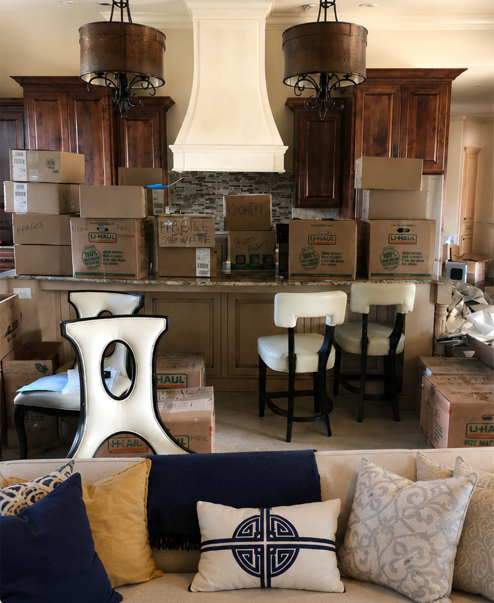 Kitchen packed with moving boxes, stools, and packed cabinets behind a sofa