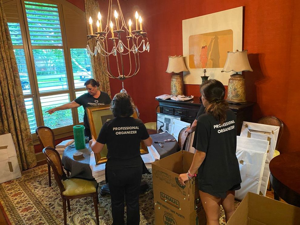 Amazing Spaces team moving boxes in a room with chandelier, lamps, and a desk by the window.