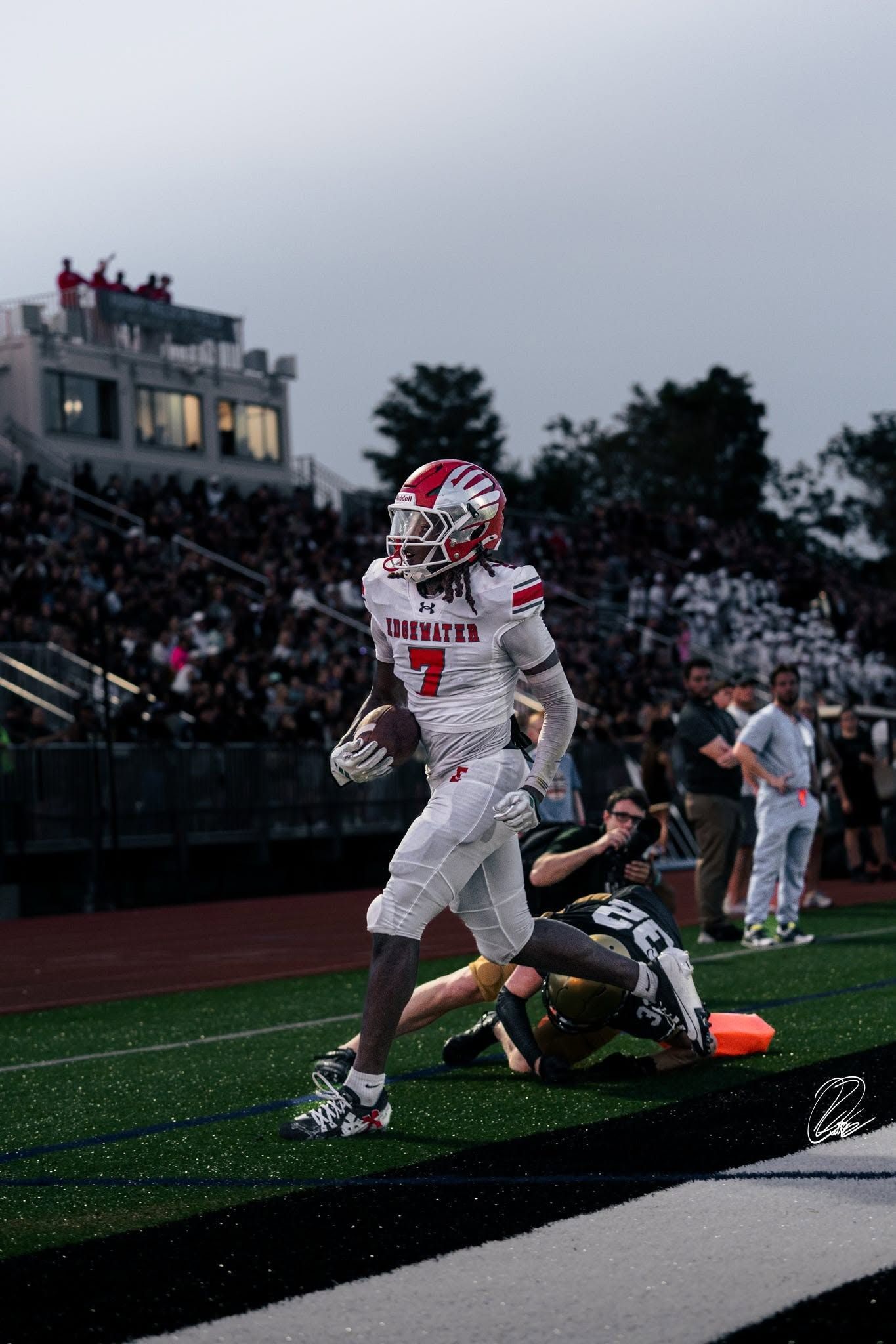 Damian Moore, Jr. in white scores a touchdown as a defender falls on the turf at dusk.