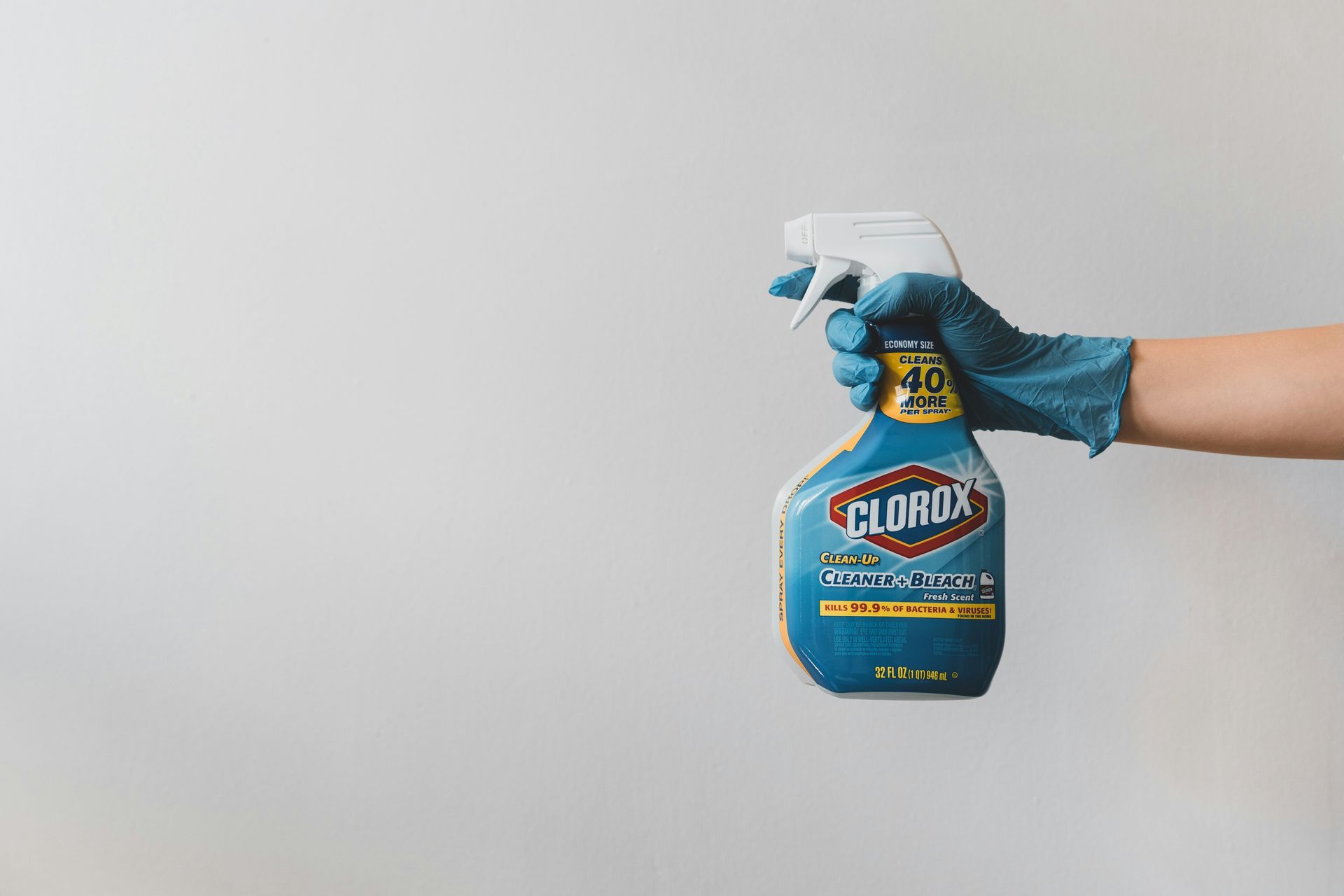 Hand in a blue glove holding a blue and white Clorox spray bottle against a white background.