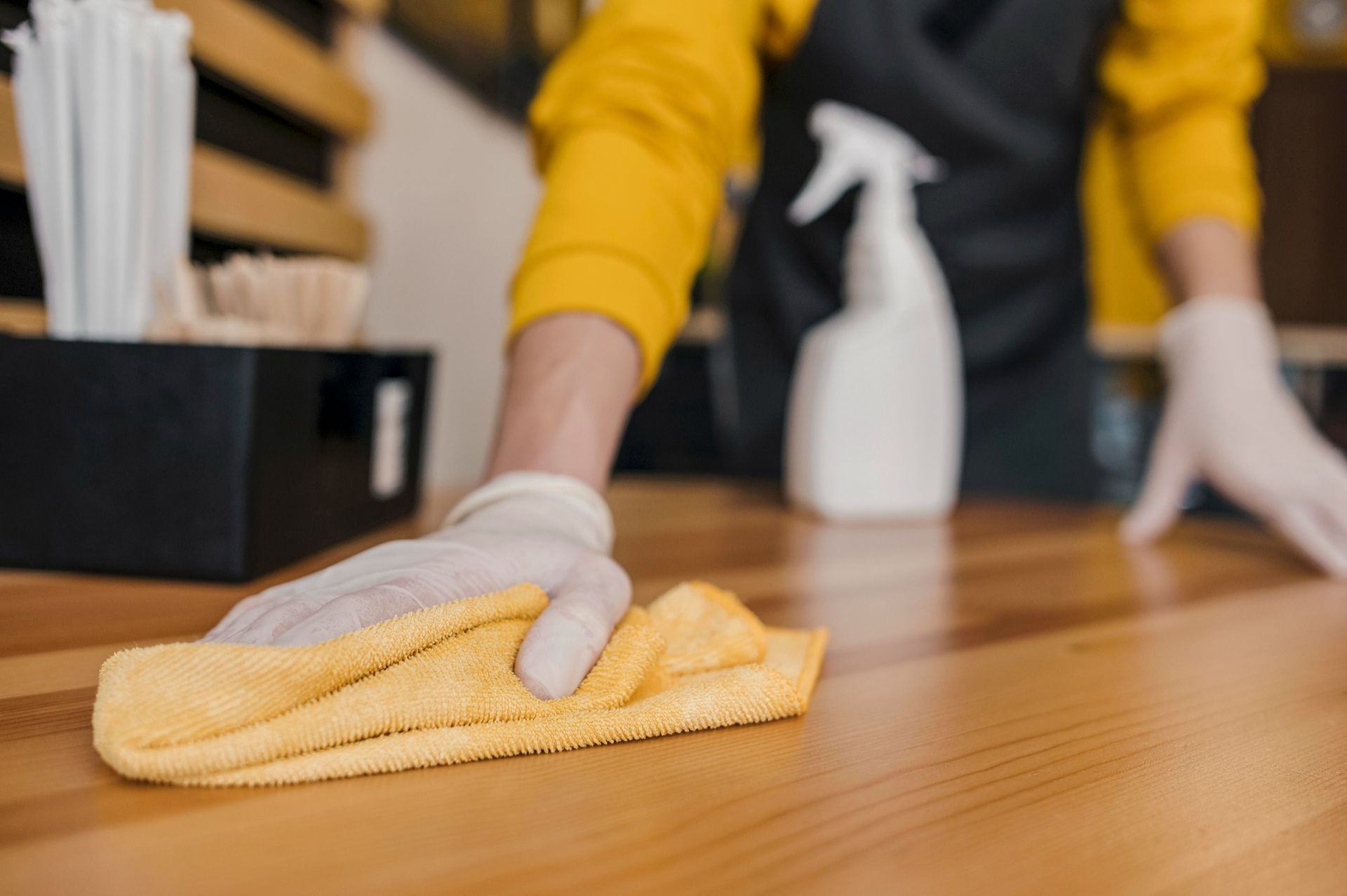 Person wiping a wooden table with a yellow cloth in a cleaning setting
