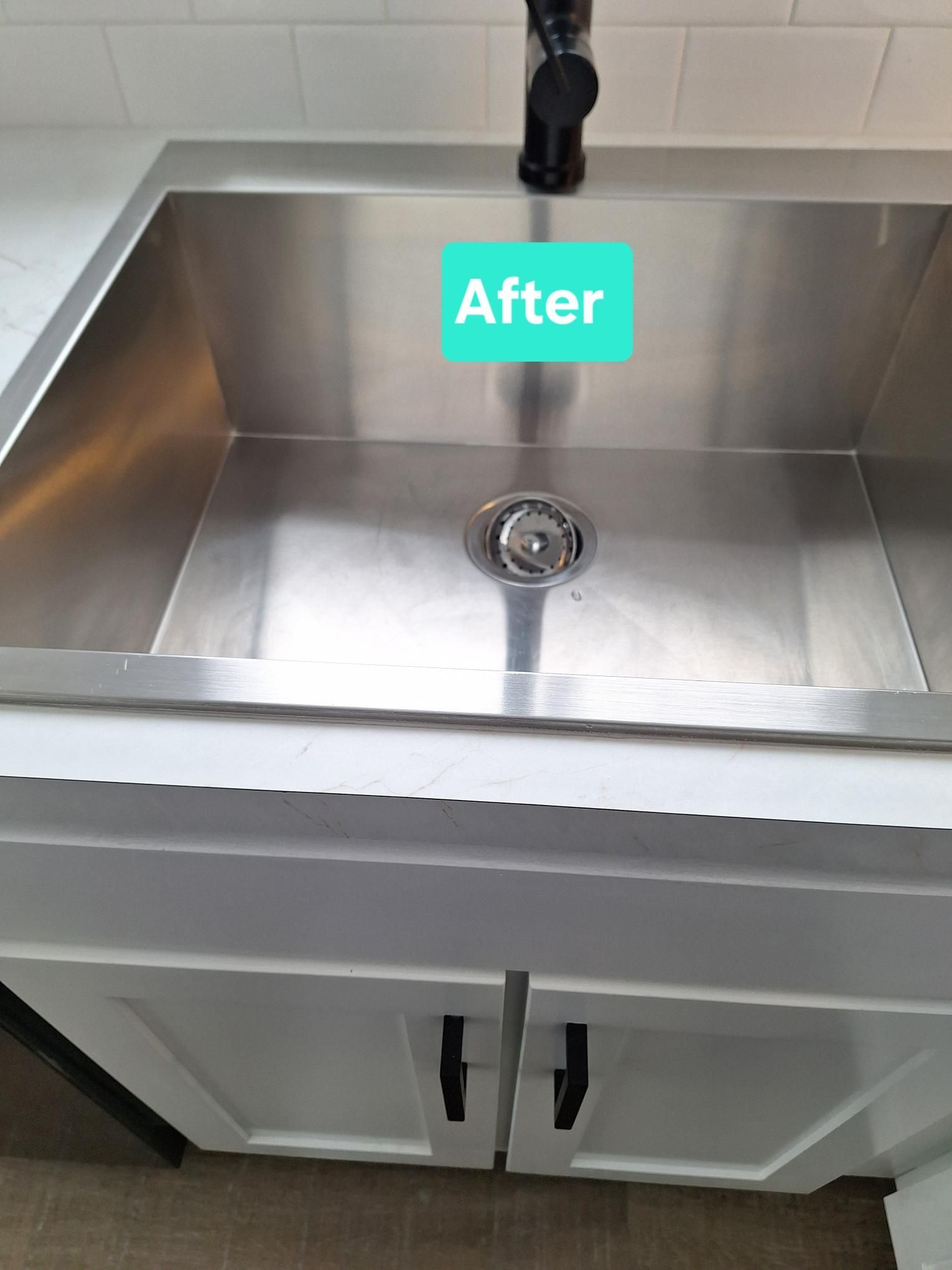 Clean stainless steel kitchen sink with black faucet, white cabinets and countertop, labeled 