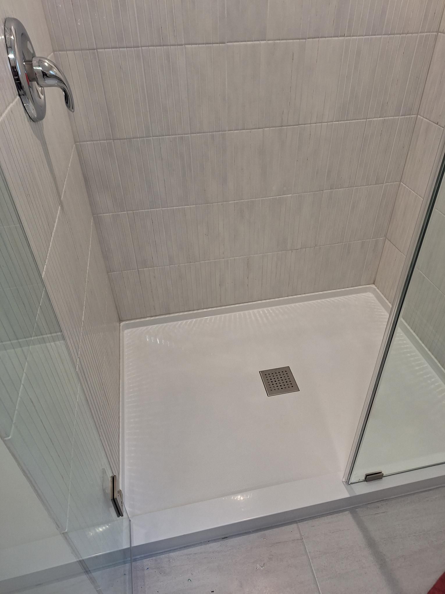A white walk-in shower stall with textured tiled walls and a glass door, viewed from above.