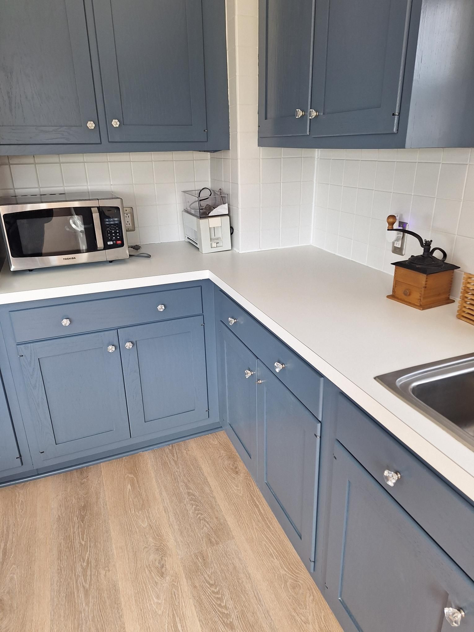 Blue kitchen cabinets with white countertops, subway tile backsplash, and microwave.