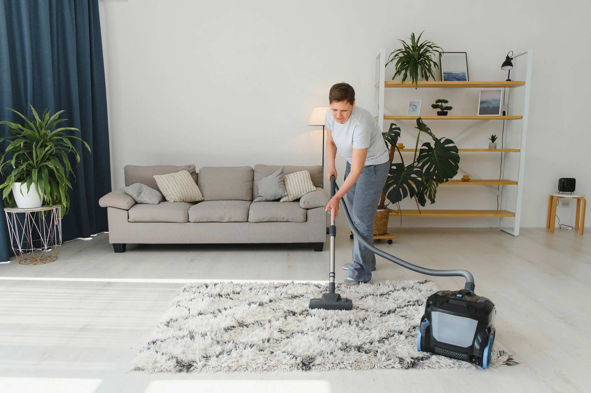Man vacuuming a white rug in a bright living room.