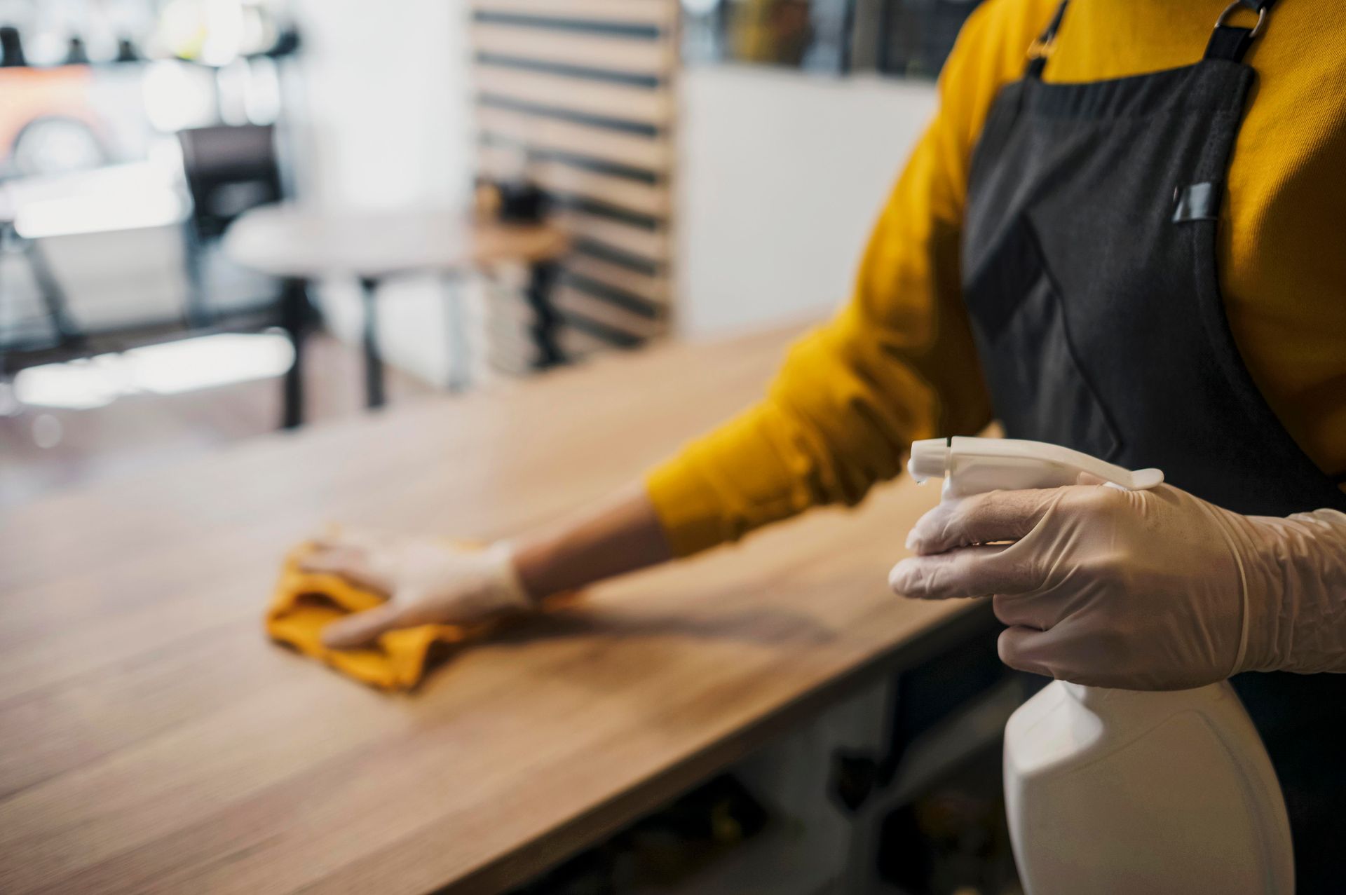 Person wearing gloves spraying and wiping down a wooden counter.