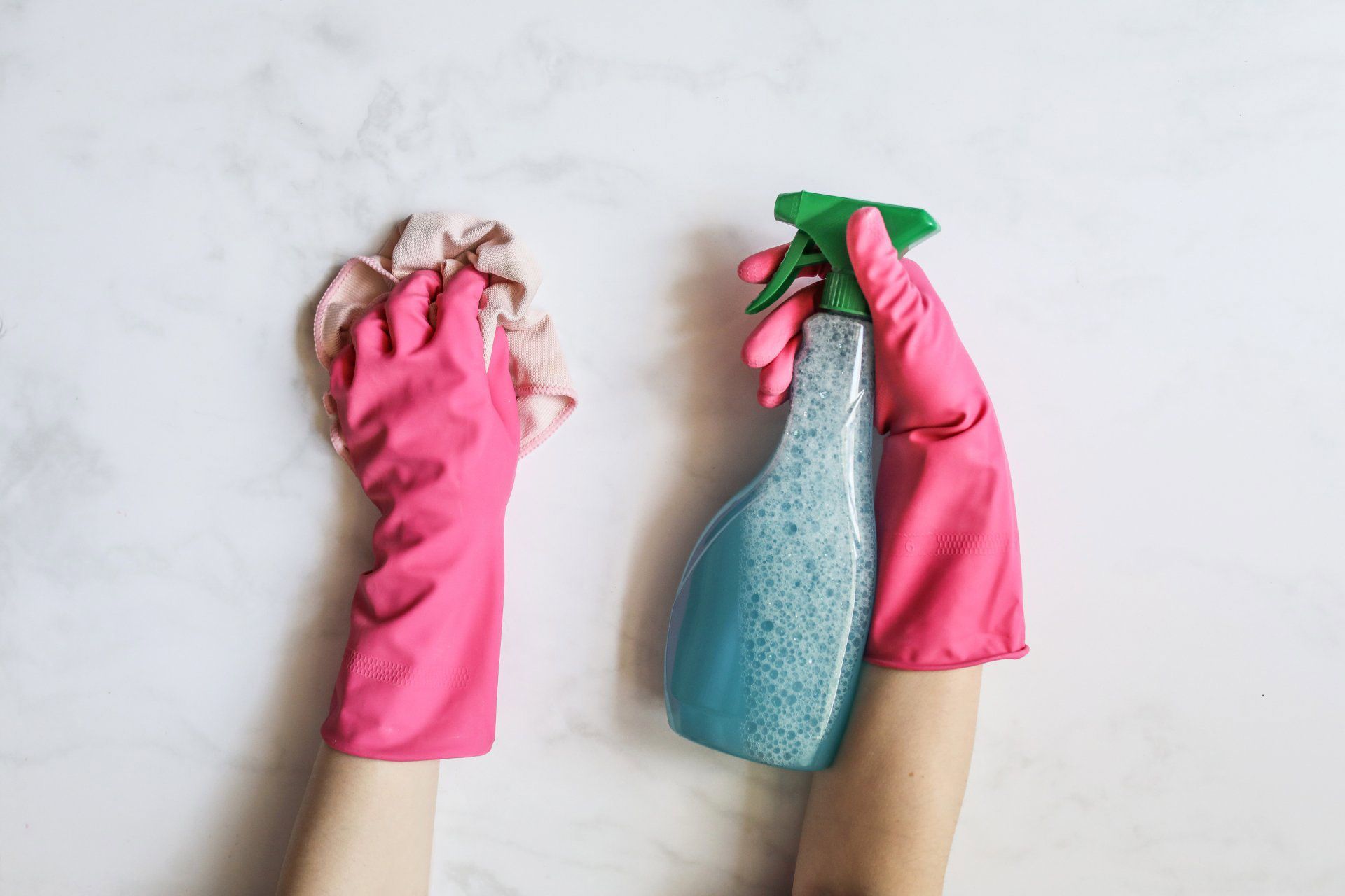 Hands in pink rubber gloves cleaning a wall with a sponge and spray bottle