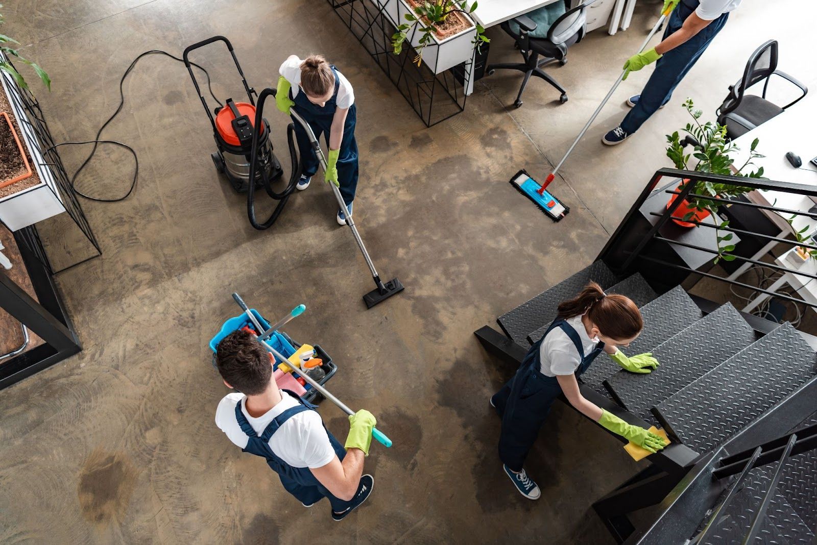 Cleaning crew in blue uniforms cleaning an office with vacuum, mop, and wiping tools.