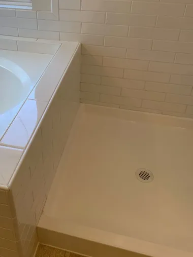 Empty white bathtub with tiled surround and shower drain in a bathroom