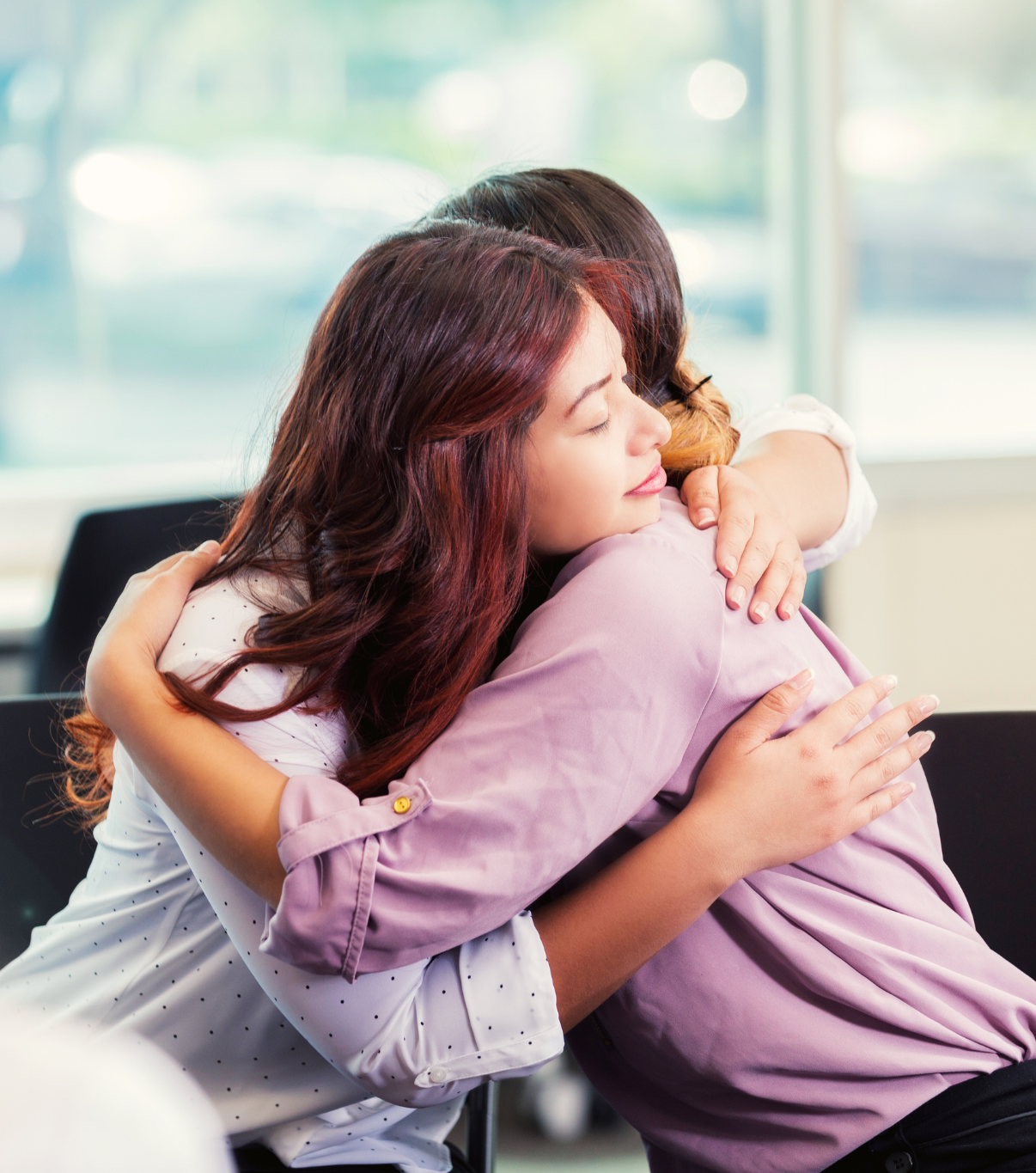 Two women embrace, indoors. One with red hair, smiling.