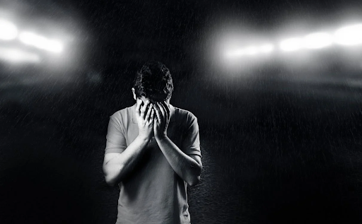 A man is covering his face with his hands in a dark room.