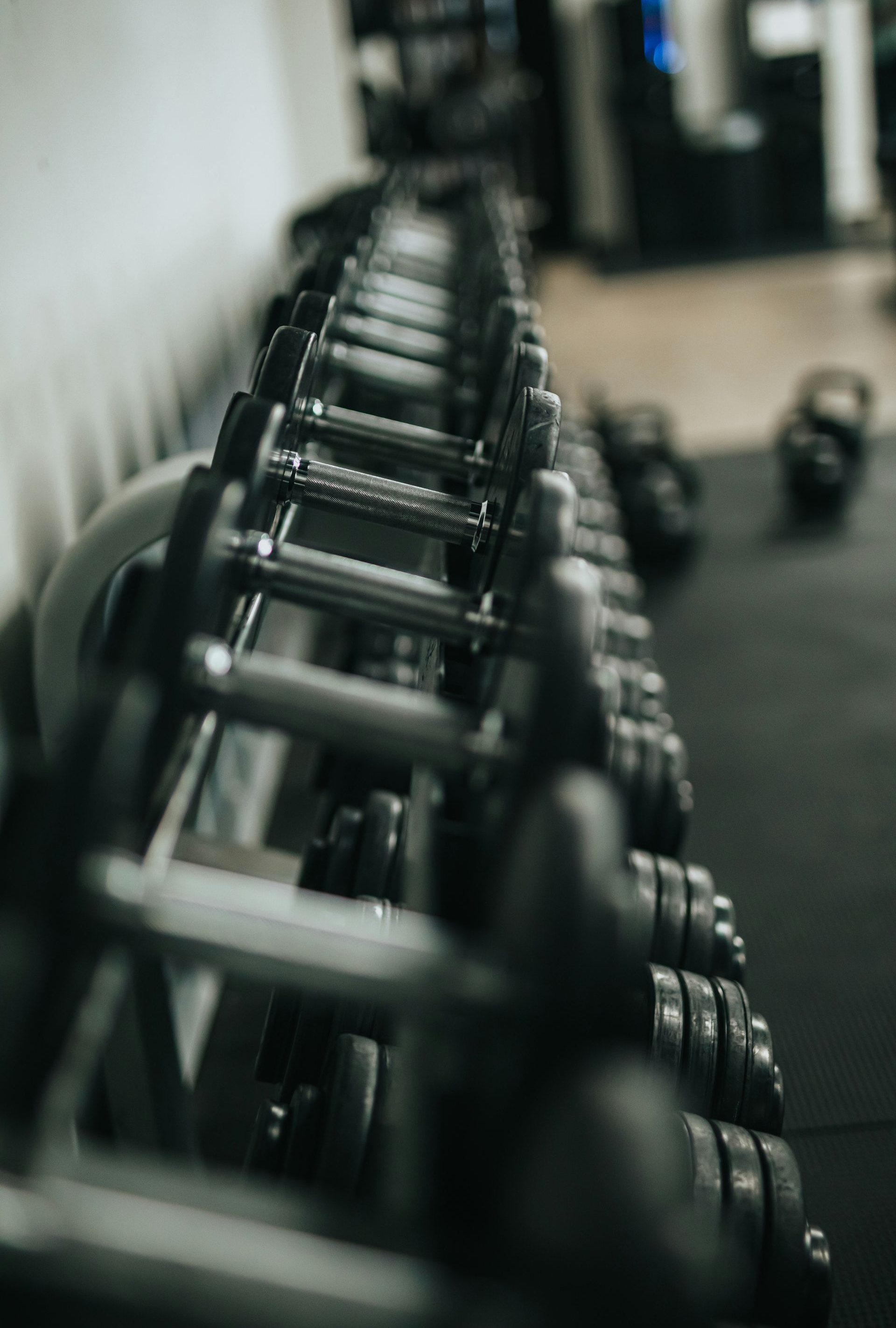 Dumbbell rack in a gym, many weights lined up. Focus on the metal weights and bars; background is dark.