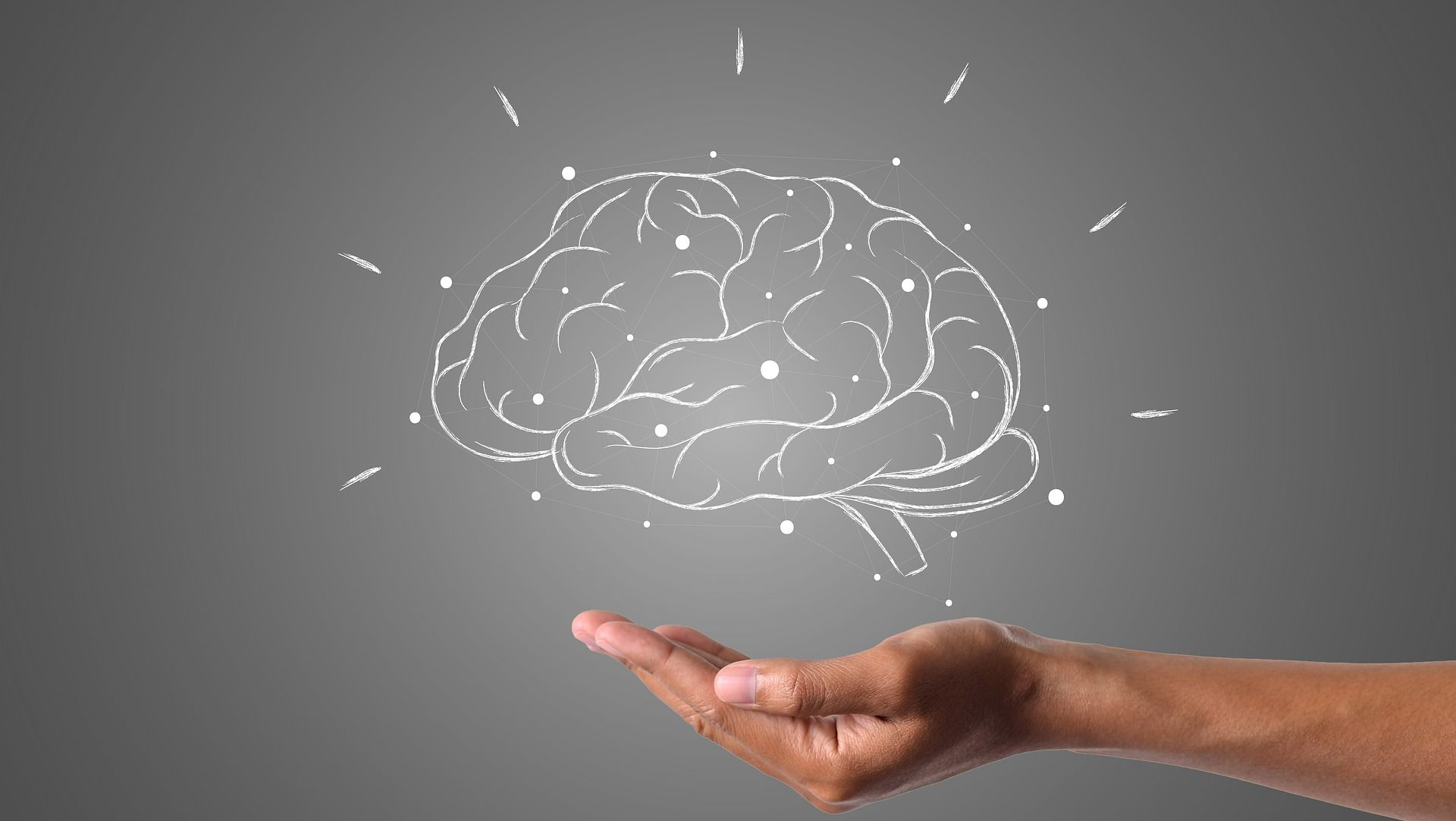 Hand holding a glowing brain illustration on a gray background.