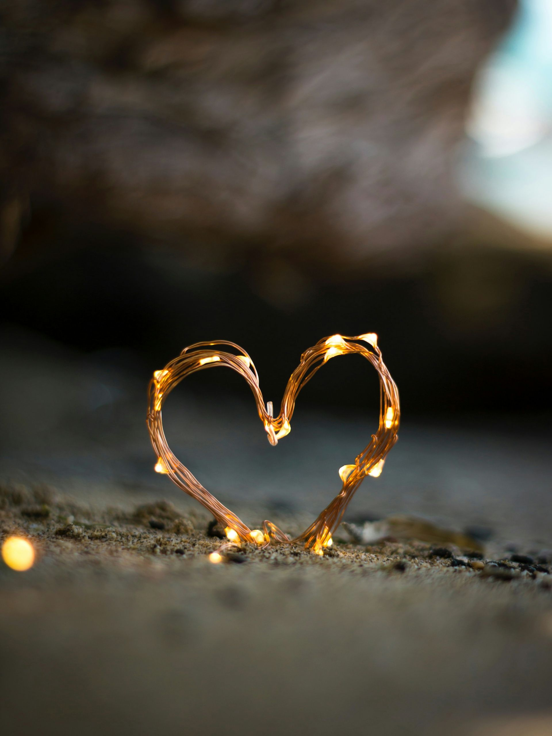 Heart-shaped decoration made of twigs, lit with small yellow lights, on a rough, dark surface.