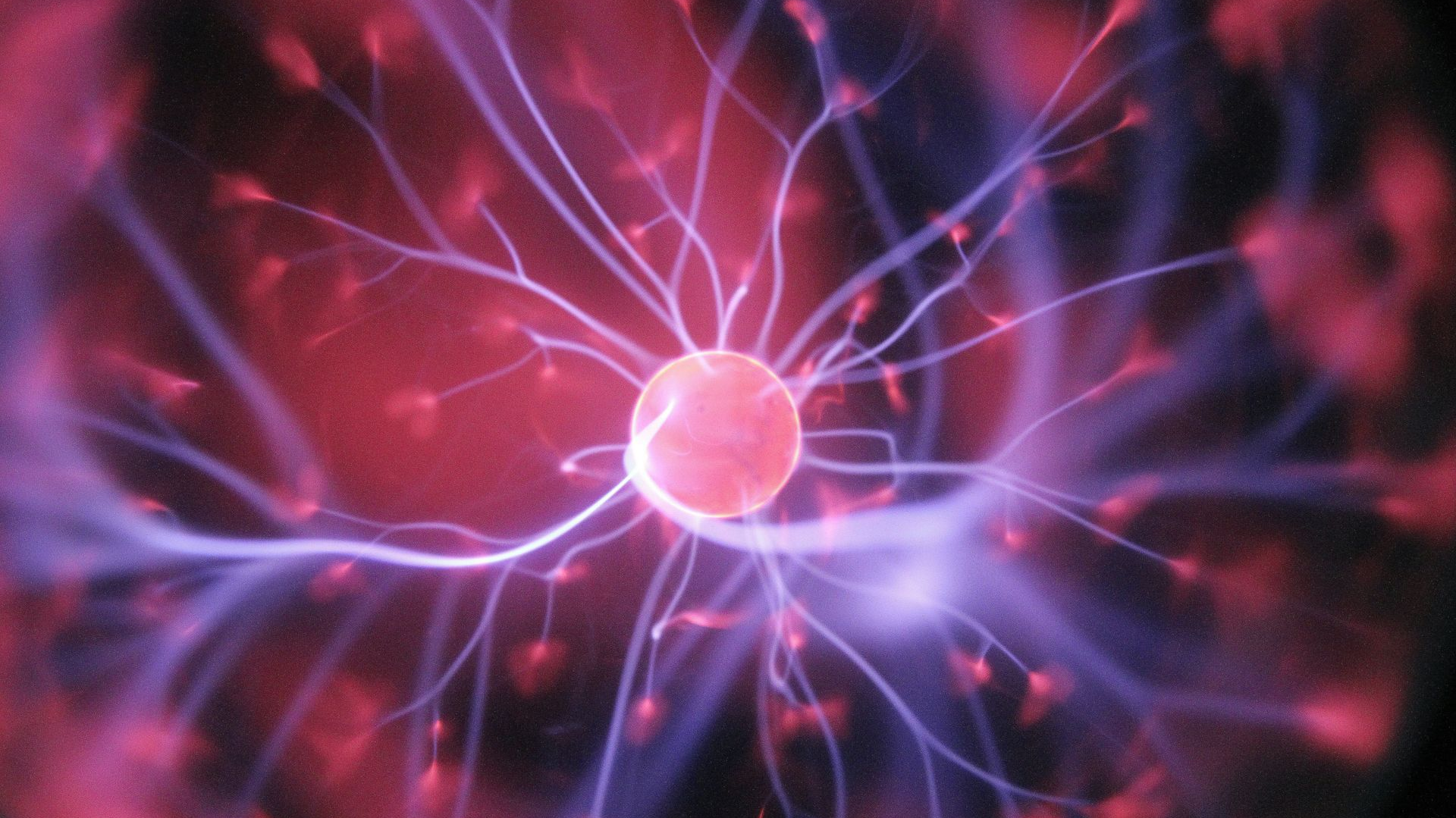A glowing plasma ball with electric purple tendrils radiating outward from a central orb, in a red, dark environment.
