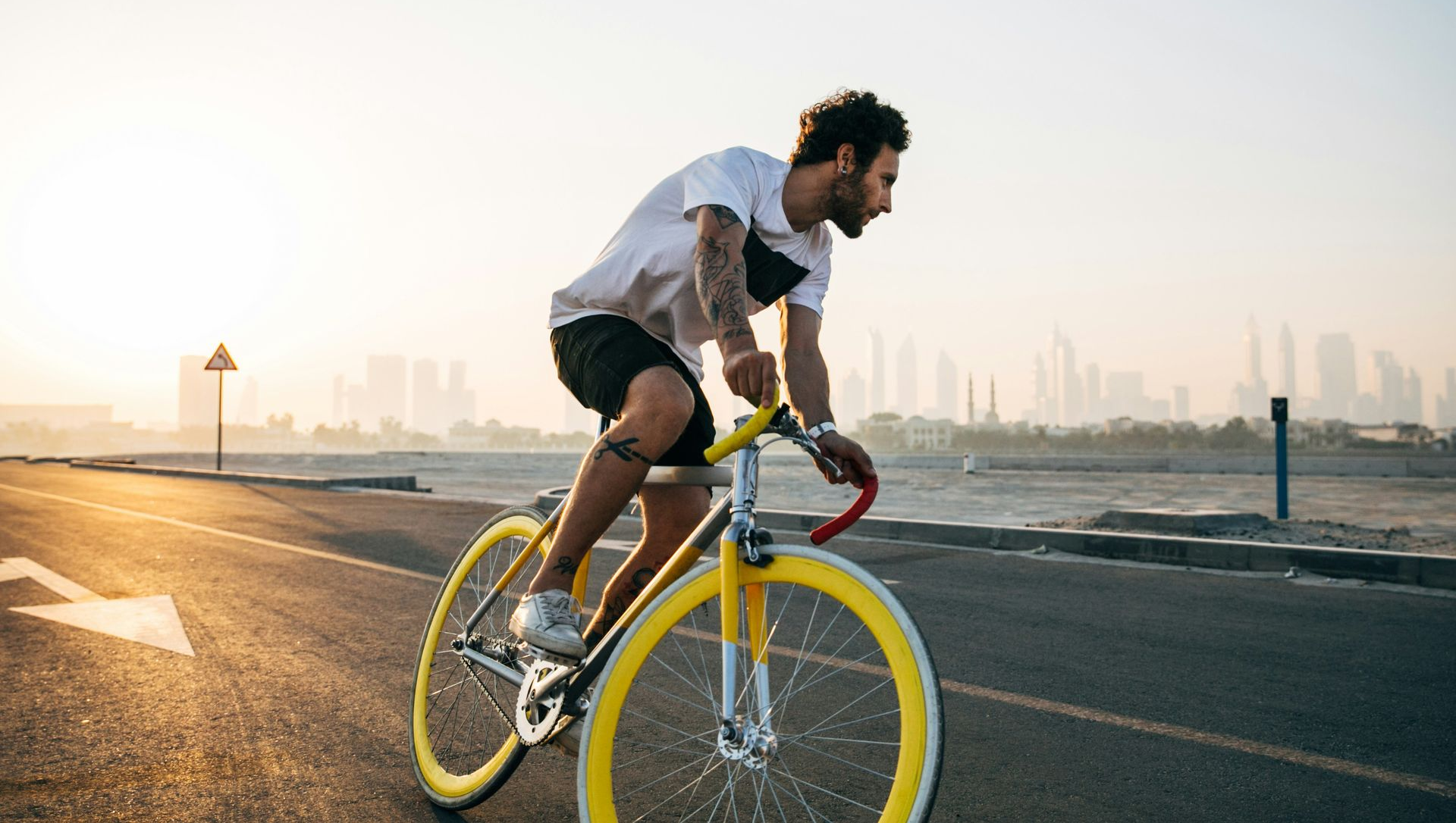 Man riding a yellow bicycle on an open road, city skyline in background.