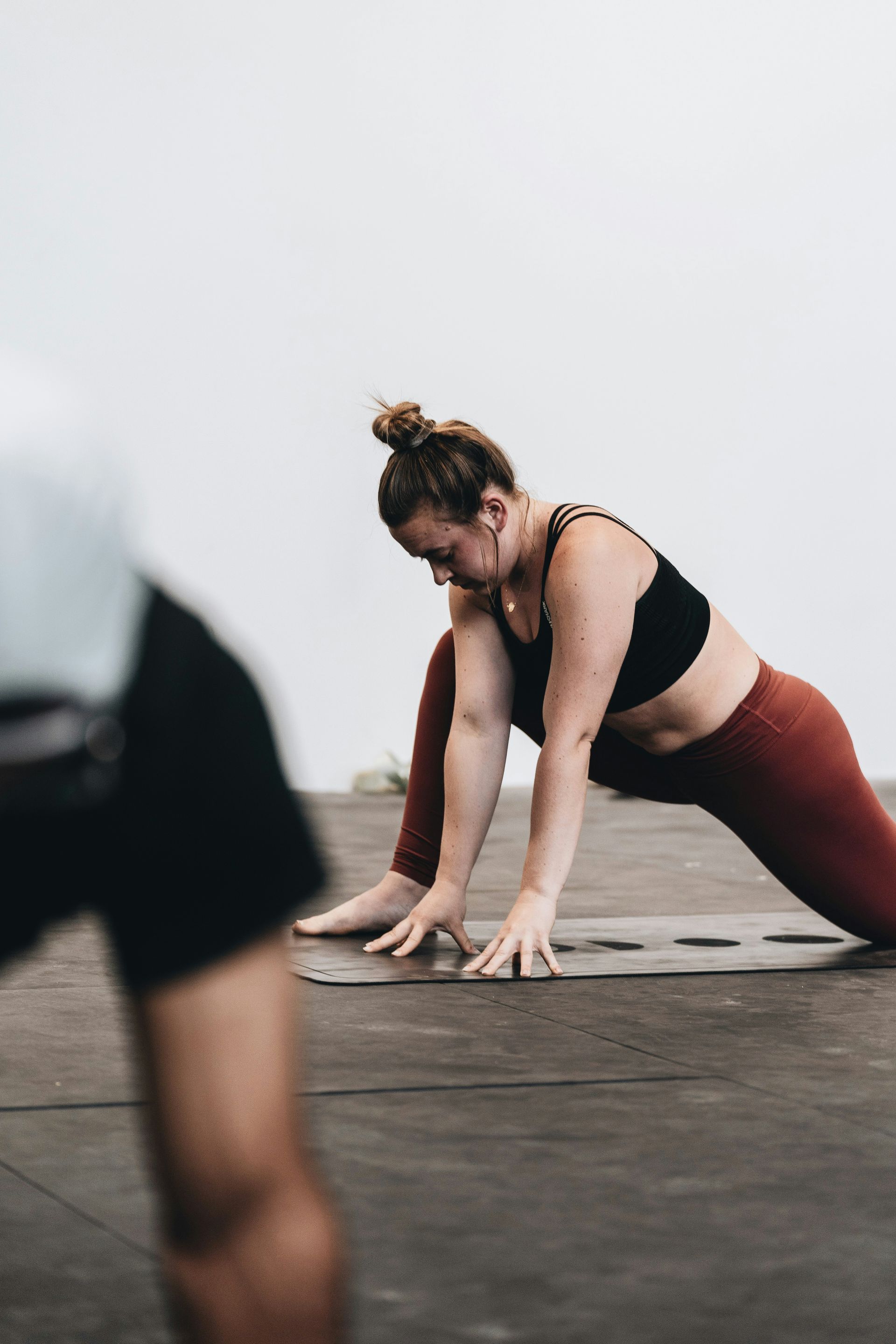 Woman in yoga pose, wearing black top, burgundy leggings, on a mat in a studio.