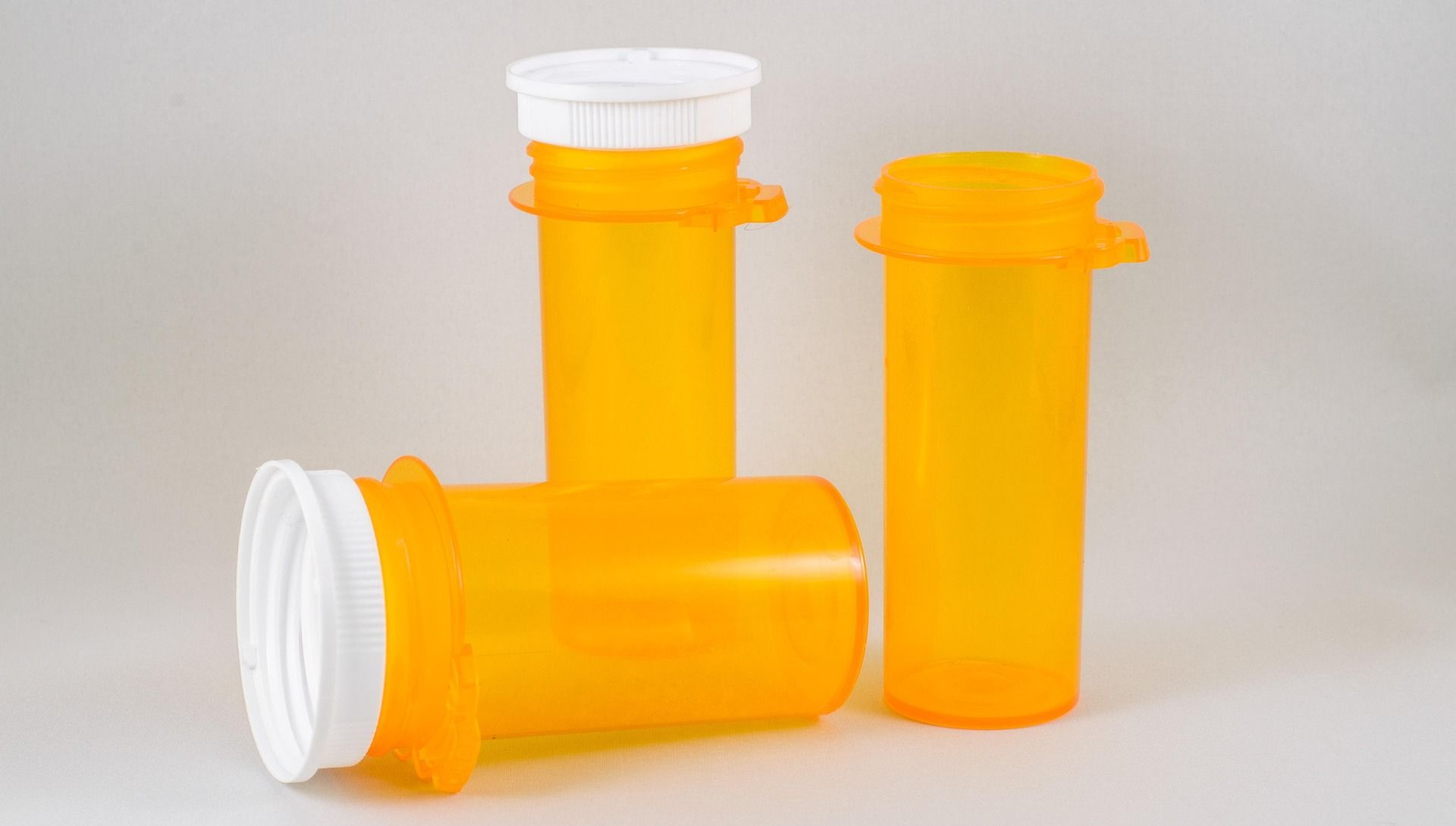 Three orange prescription pill bottles, two upright and one on its side, with white child-proof caps.