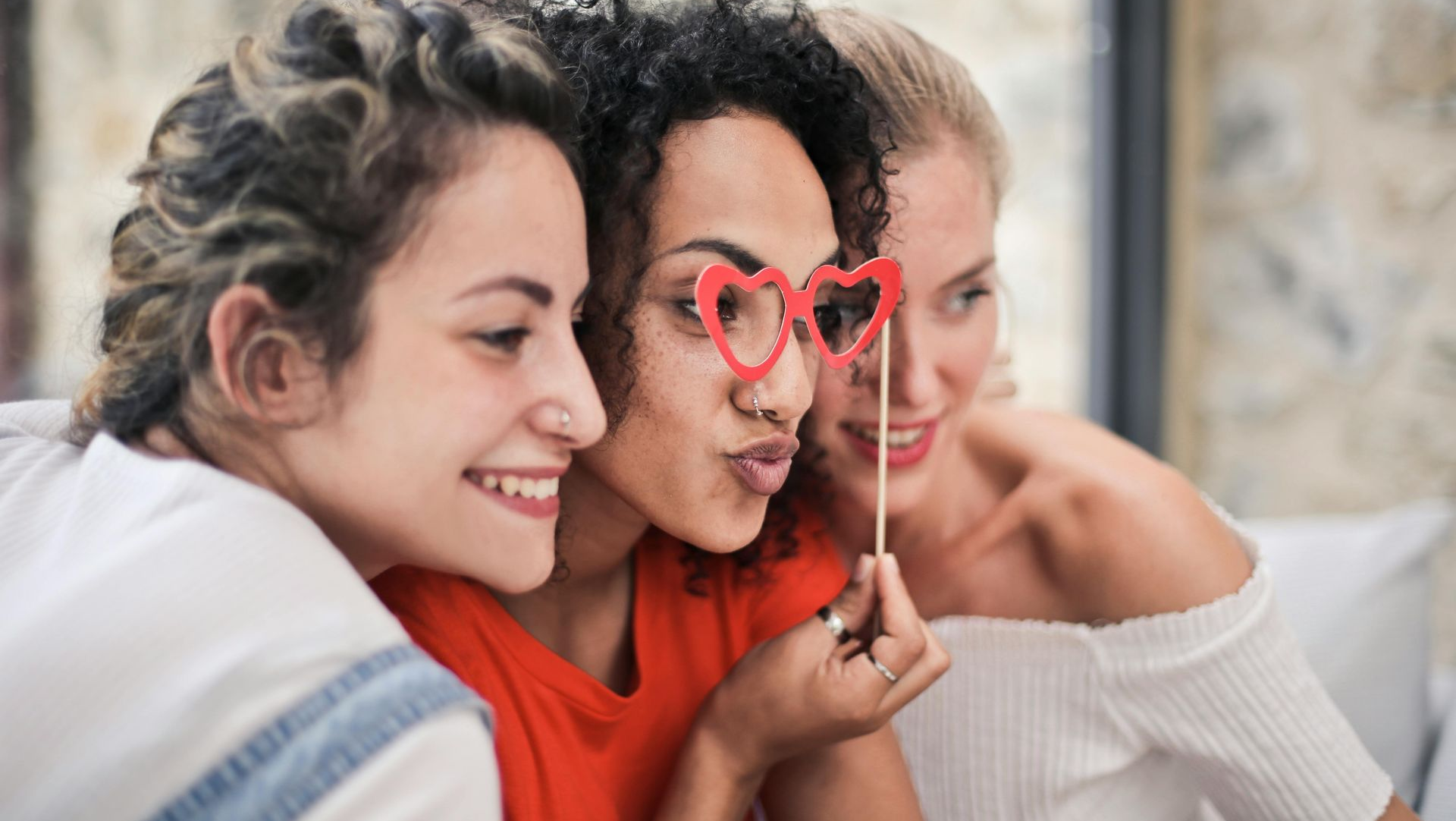 Three people posing together; one holds heart-shaped prop, all smiling.