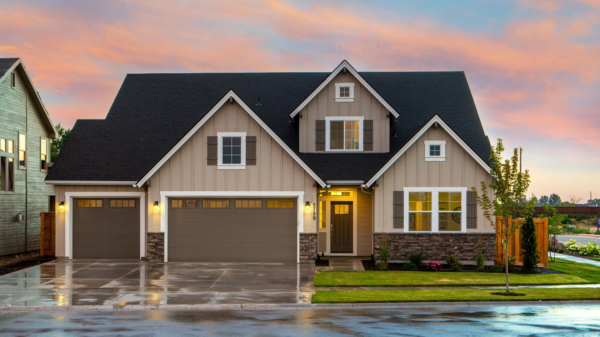 Tan house with black roof, brown garage doors, and a colorful sunset sky.