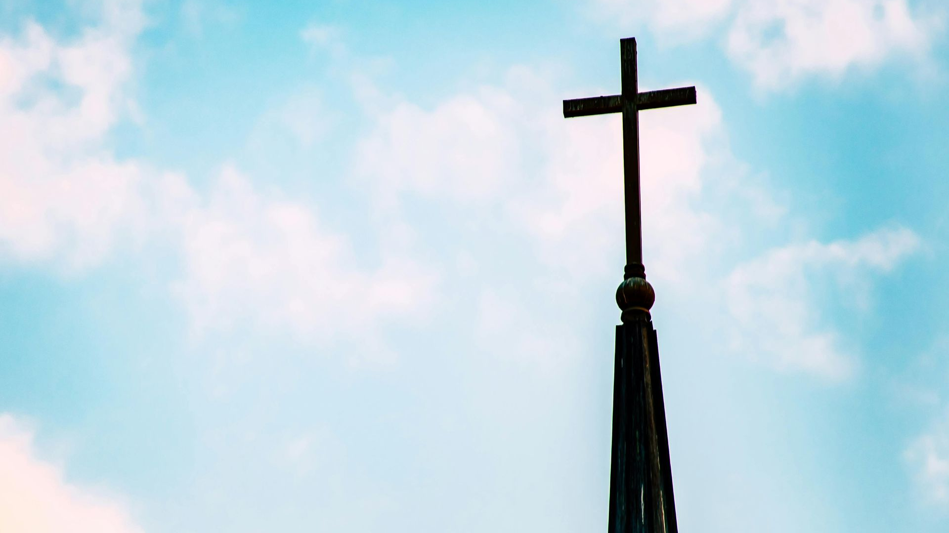 Cross on top of a church spire against a blue sky with clouds.