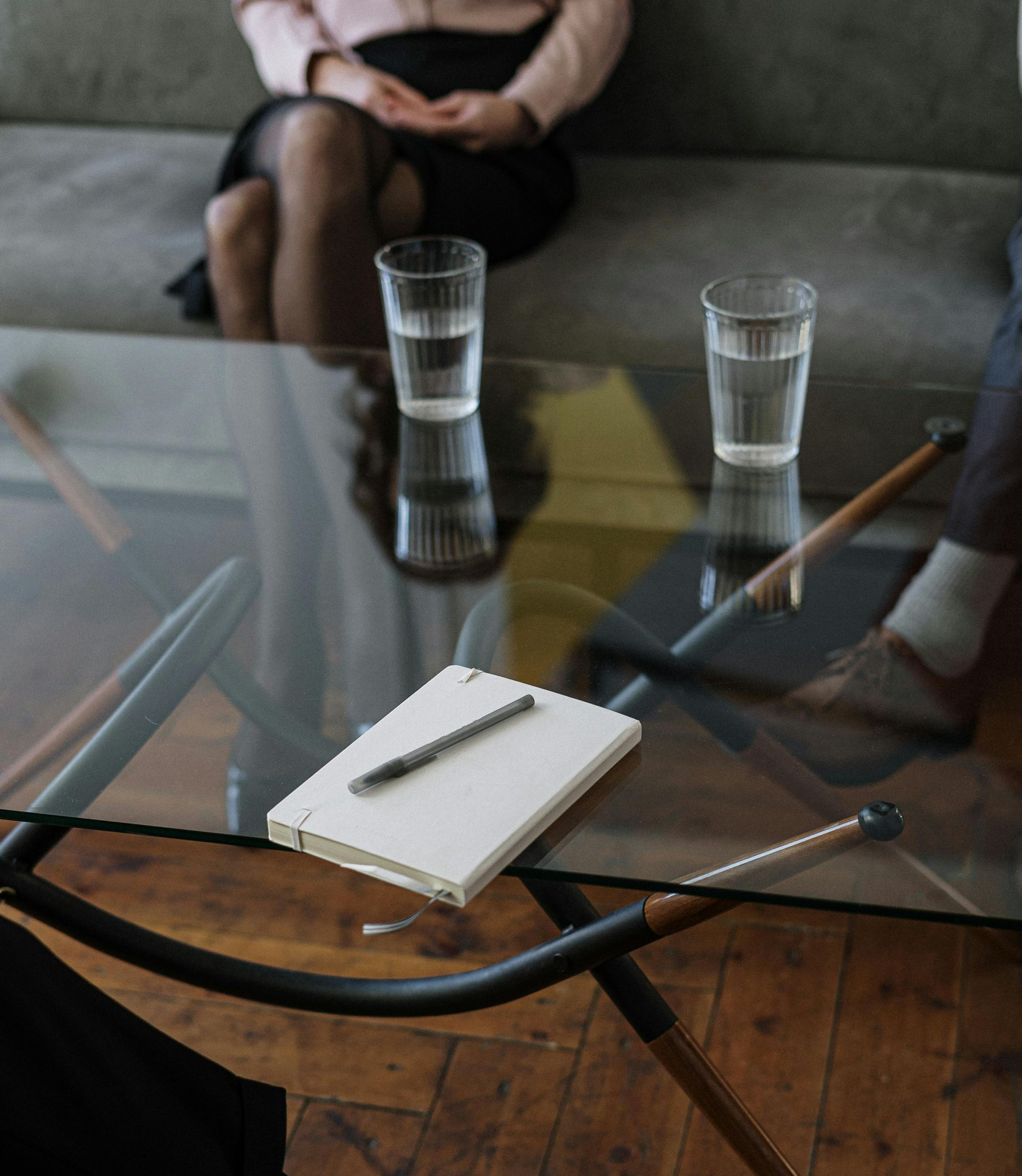 Two people in a therapy session. Notebook and glasses of water on a glass table.