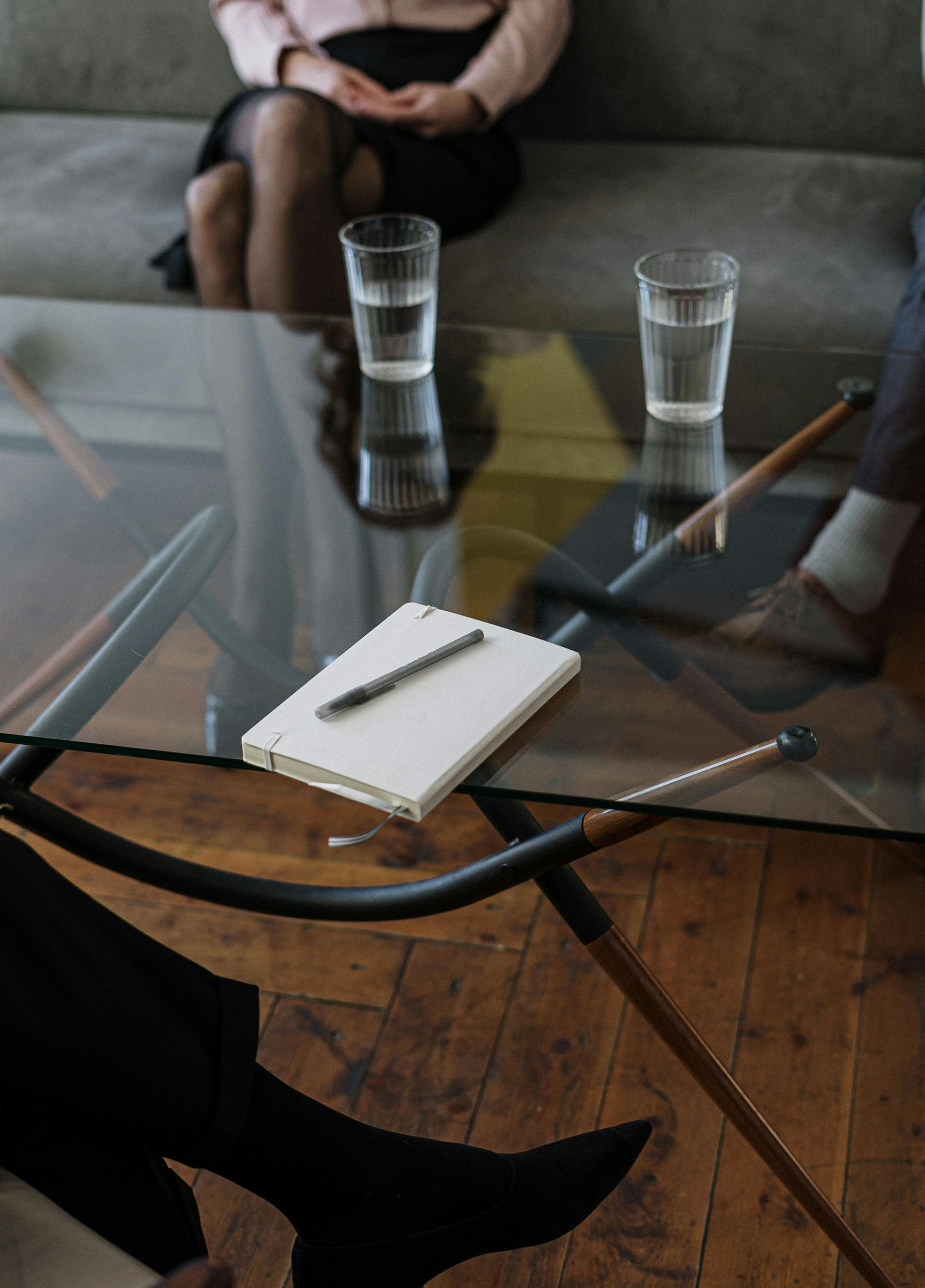 People in therapy session. Glass table with notebook, pen, and water glasses.