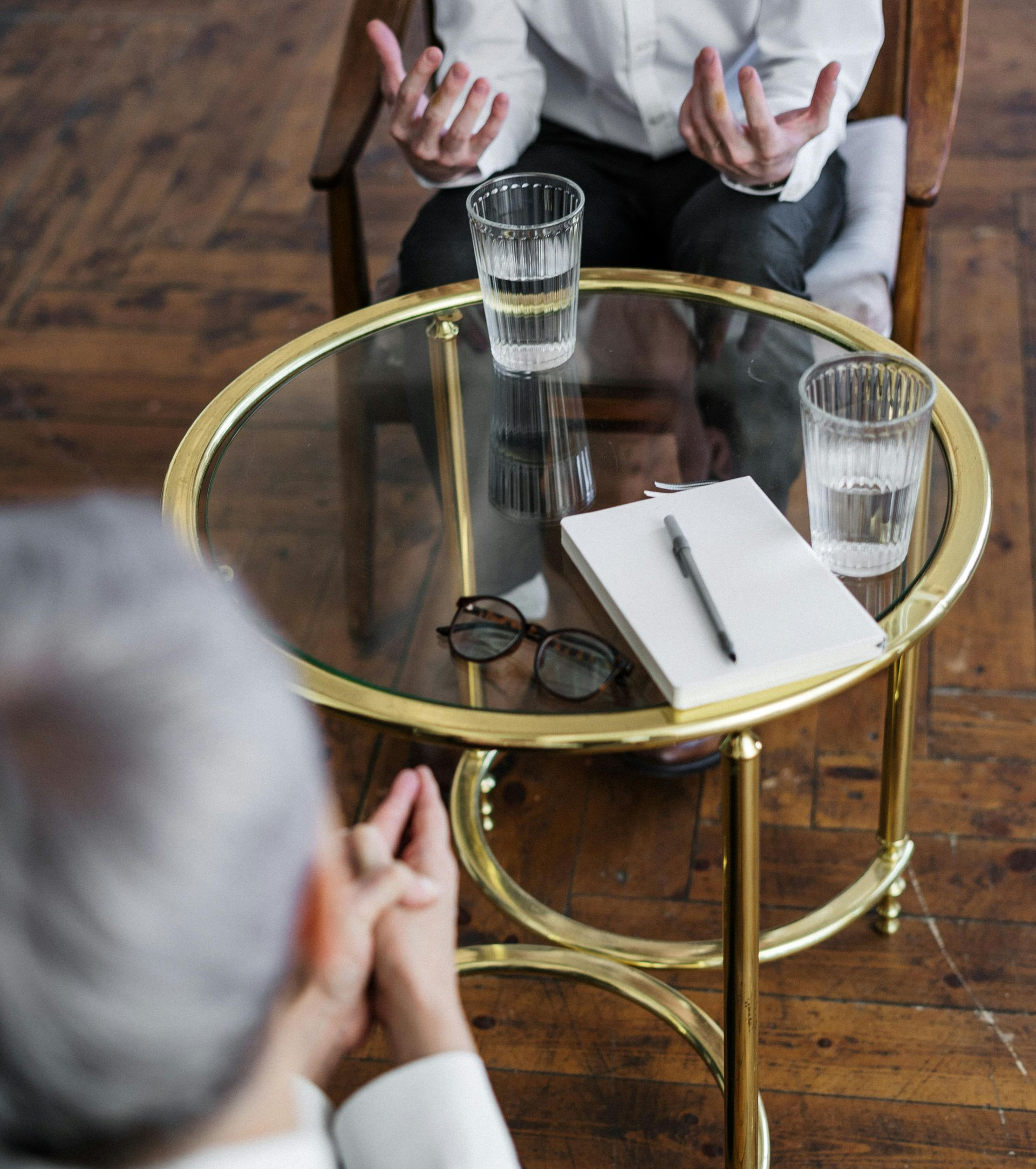 Therapist and patient in a session at a round table with water glasses and a notepad.
