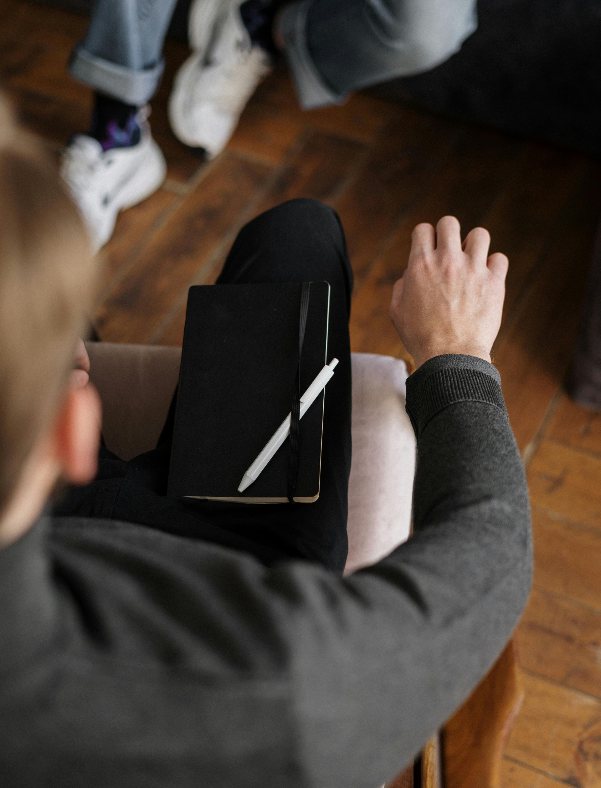 Person sitting, holding a black notebook with white line, with others in background.
