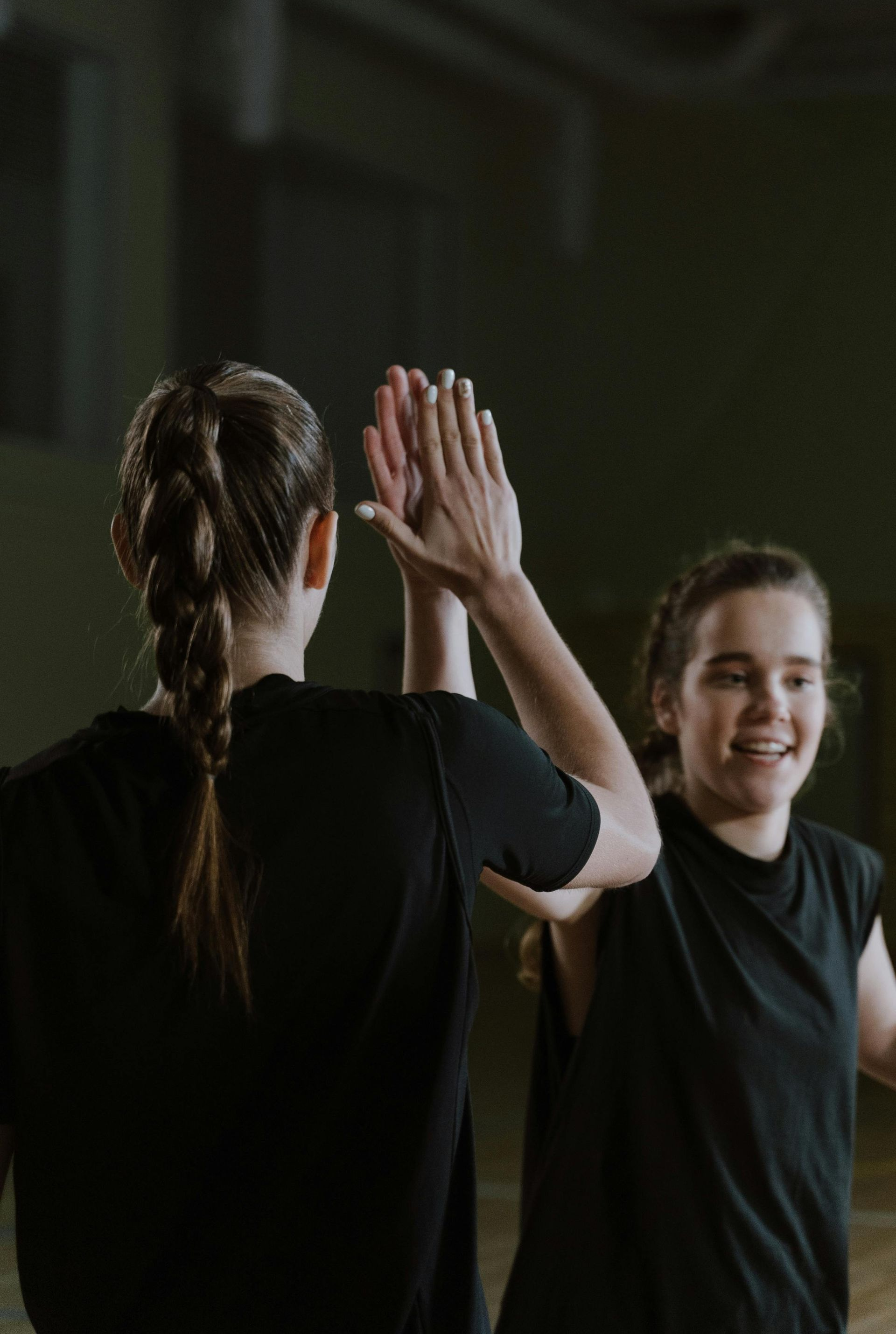Two people in black shirts high-fiving in a gymnasium, one smiling.