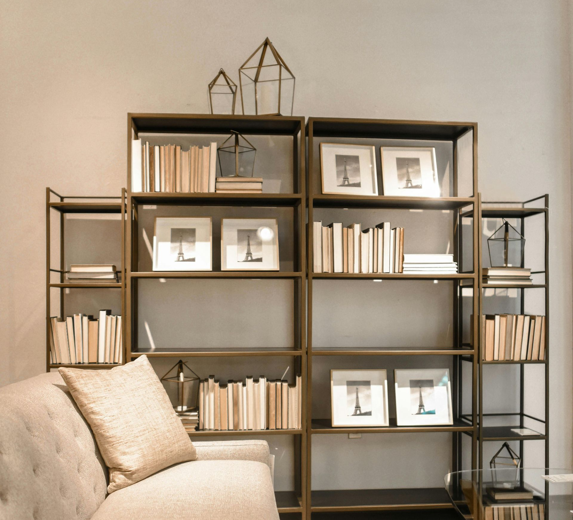 Gold metal bookshelves with books, framed art, and decorative lanterns; next to a sofa.