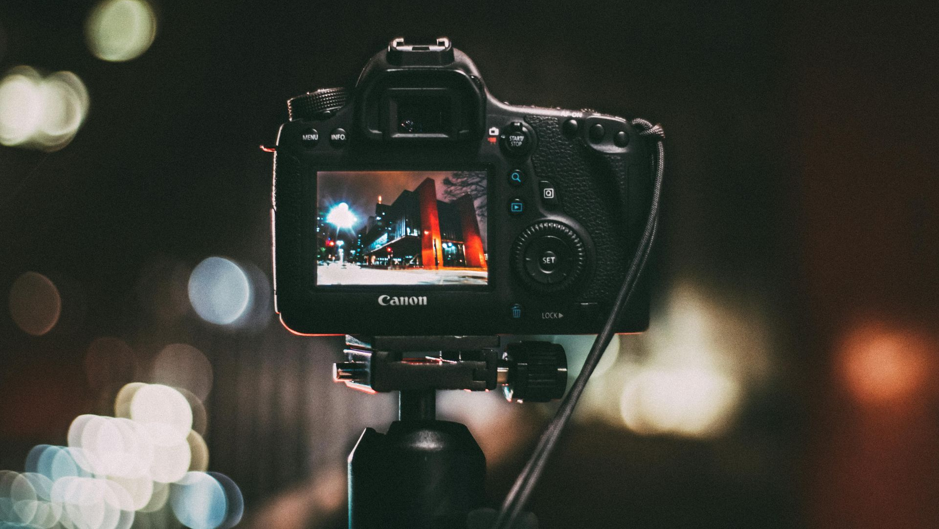 Black DSLR camera on tripod, back screen displaying a night cityscape with blurred lights.