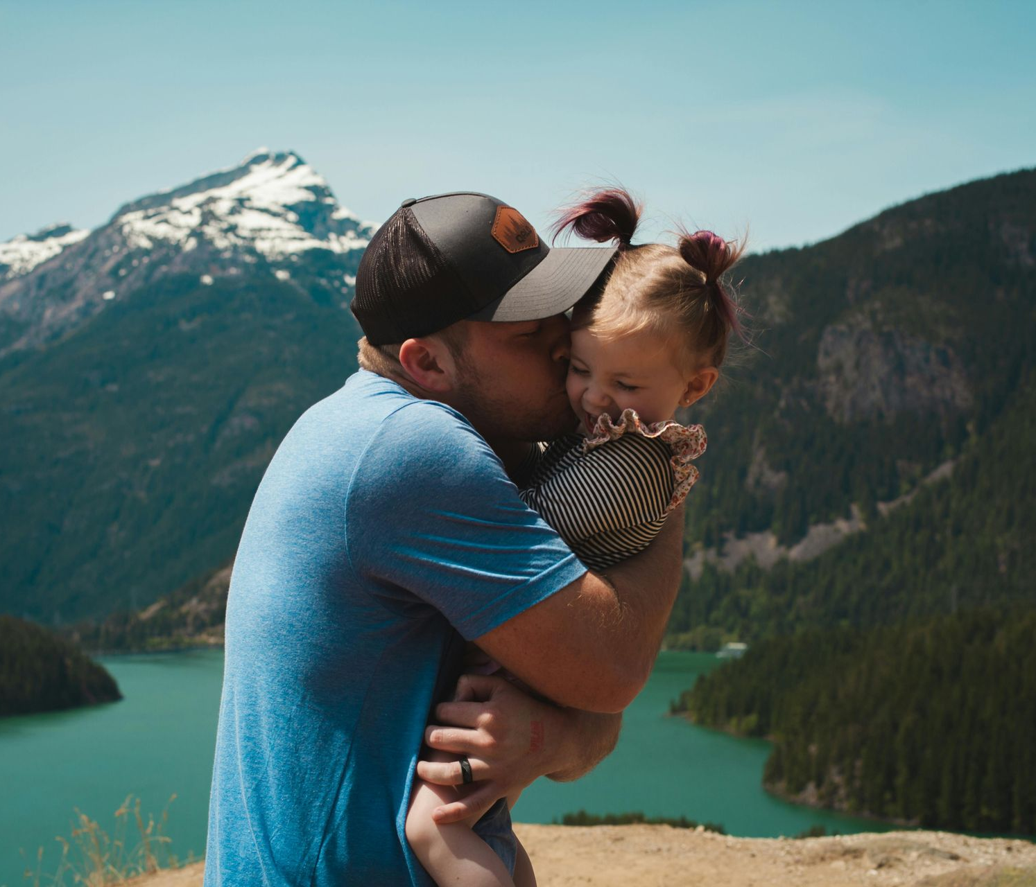 Man kissing baby's cheek, overlooking lake and mountain.