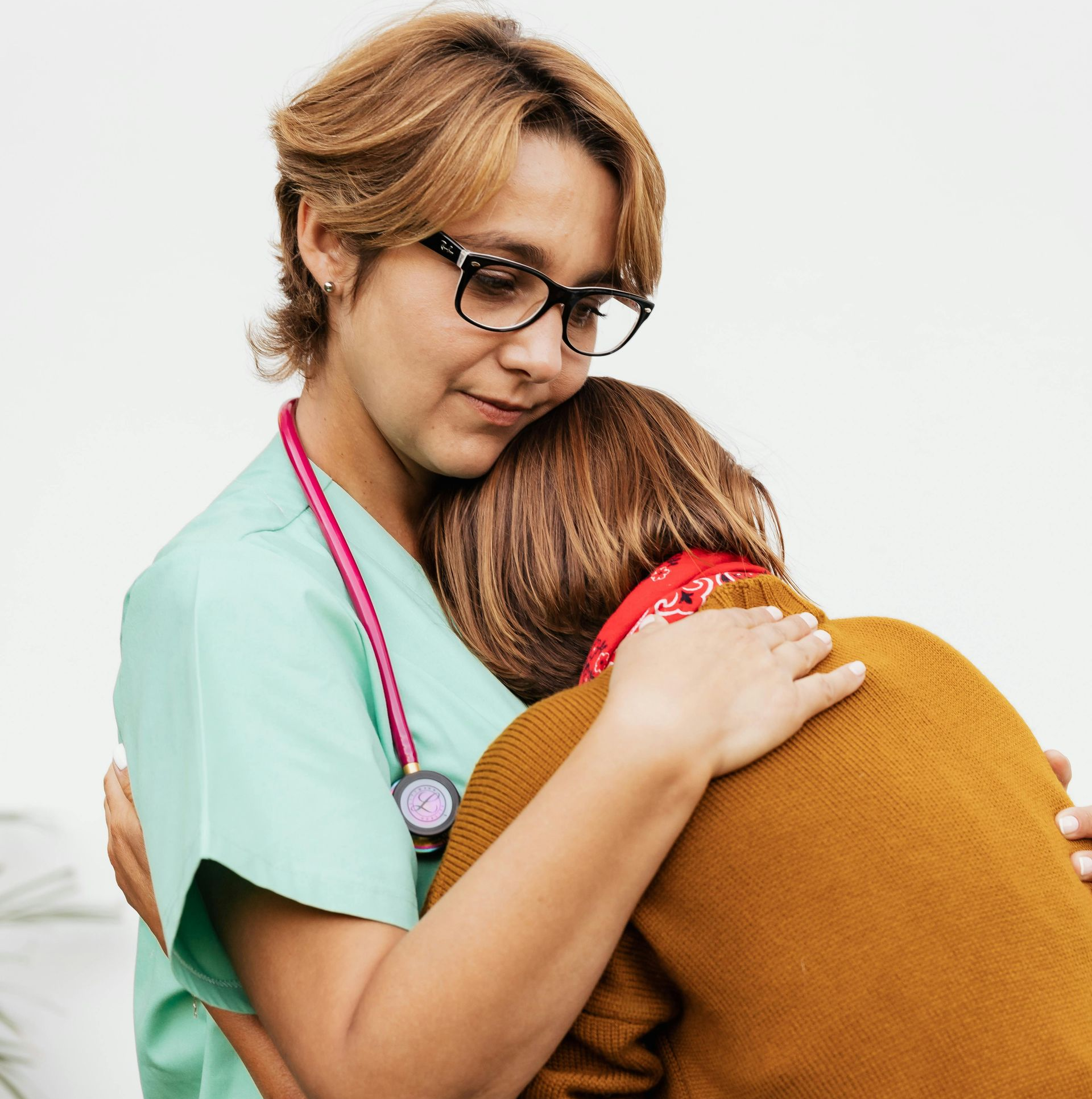 Nurse in scrubs hugs patient; stethoscope, worried expression, indoors.