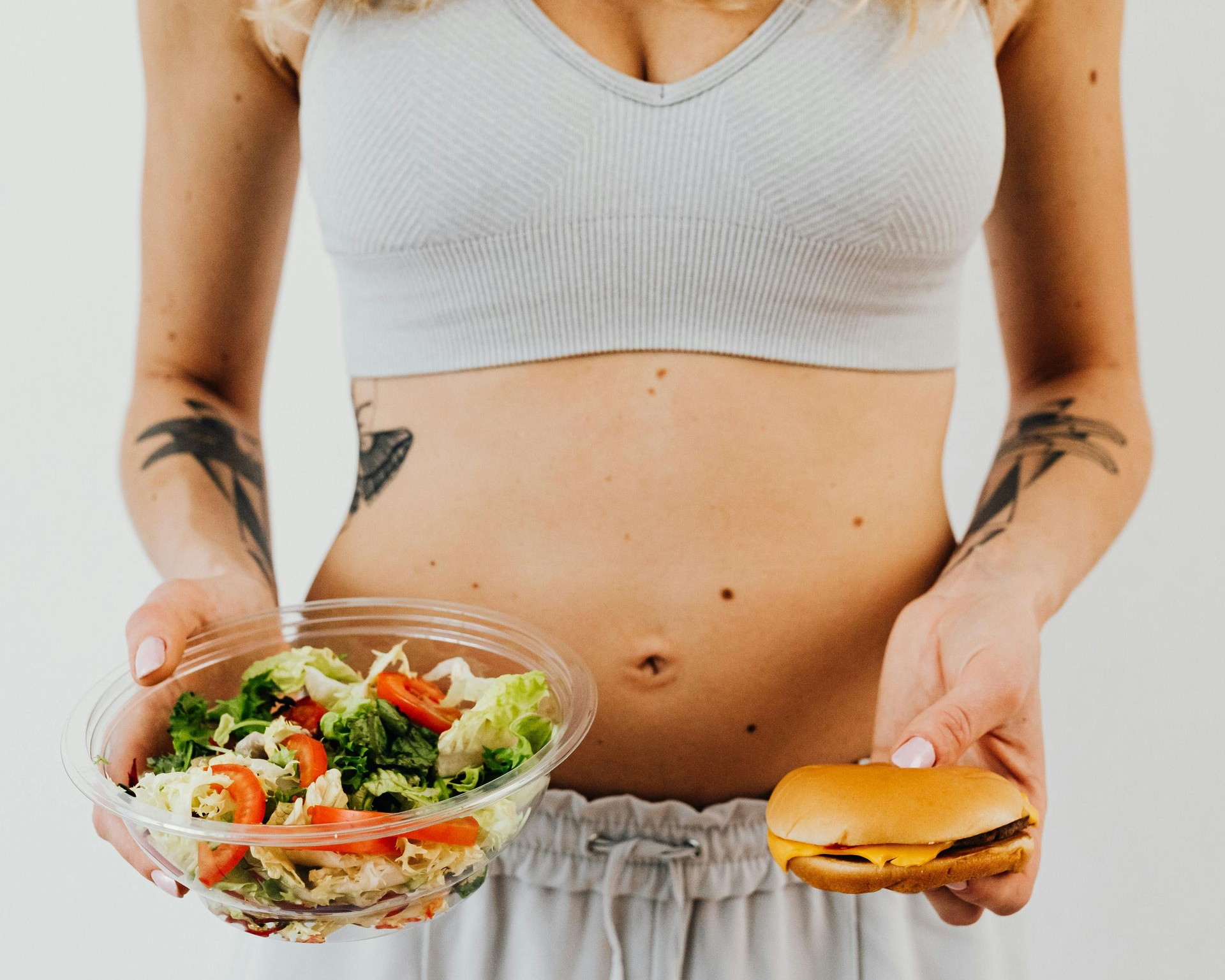 Woman holding a salad bowl and a hamburger, contrasting healthy and fast food.
