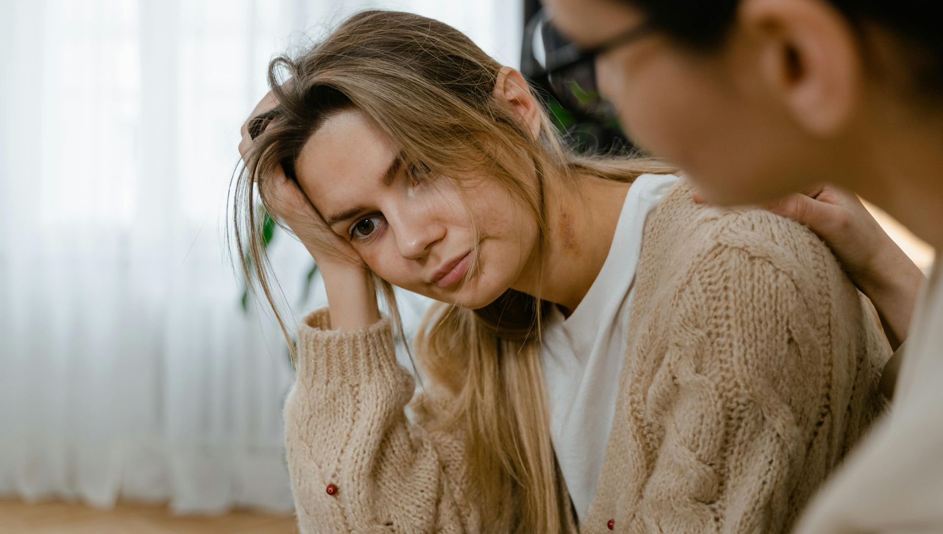Woman looking distressed as another person comforts her. Indoors, neutral colors.