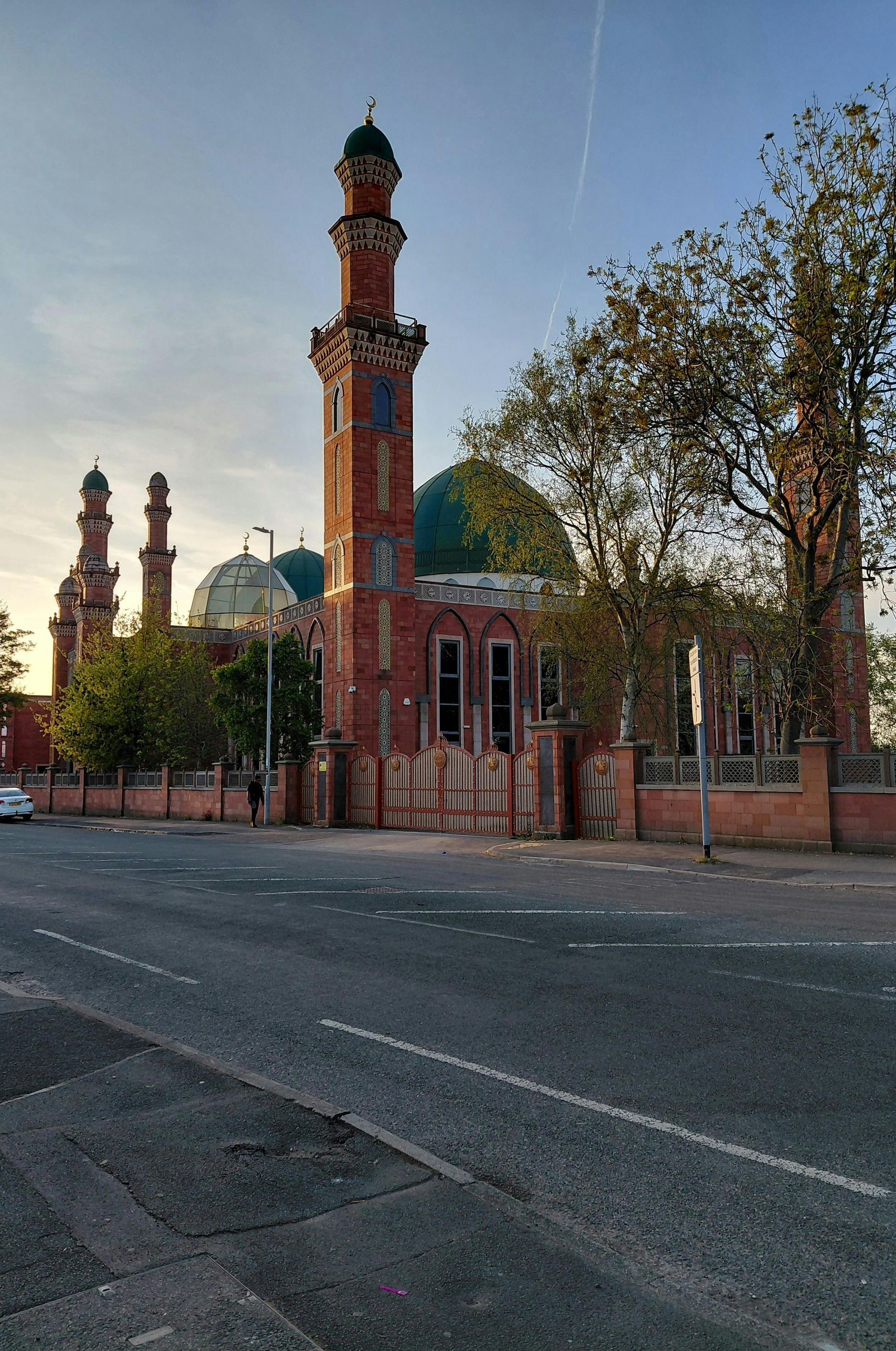 Mosque with red brick facade, green dome, and minarets; tree in front.