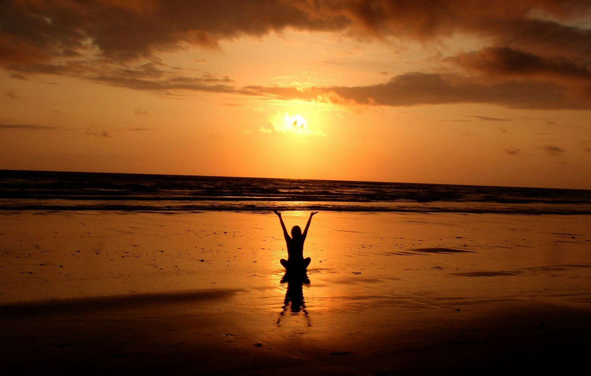 Silhouette of person with arms raised in yoga pose on beach at sunset.