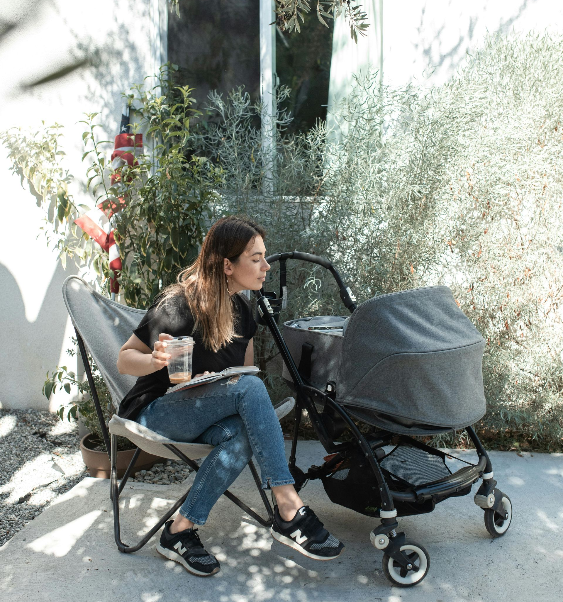 Woman sitting in a chair, with a stroller nearby, enjoying food and drink outside.
