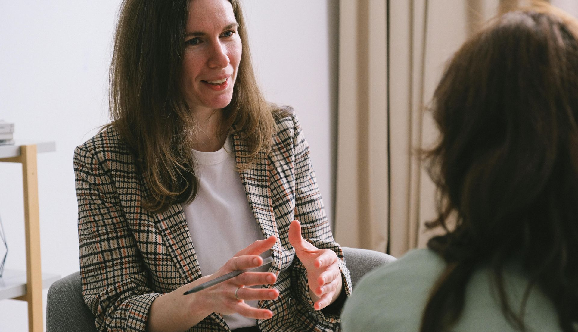 Woman in blazer gestures while talking to another person in a counseling session.